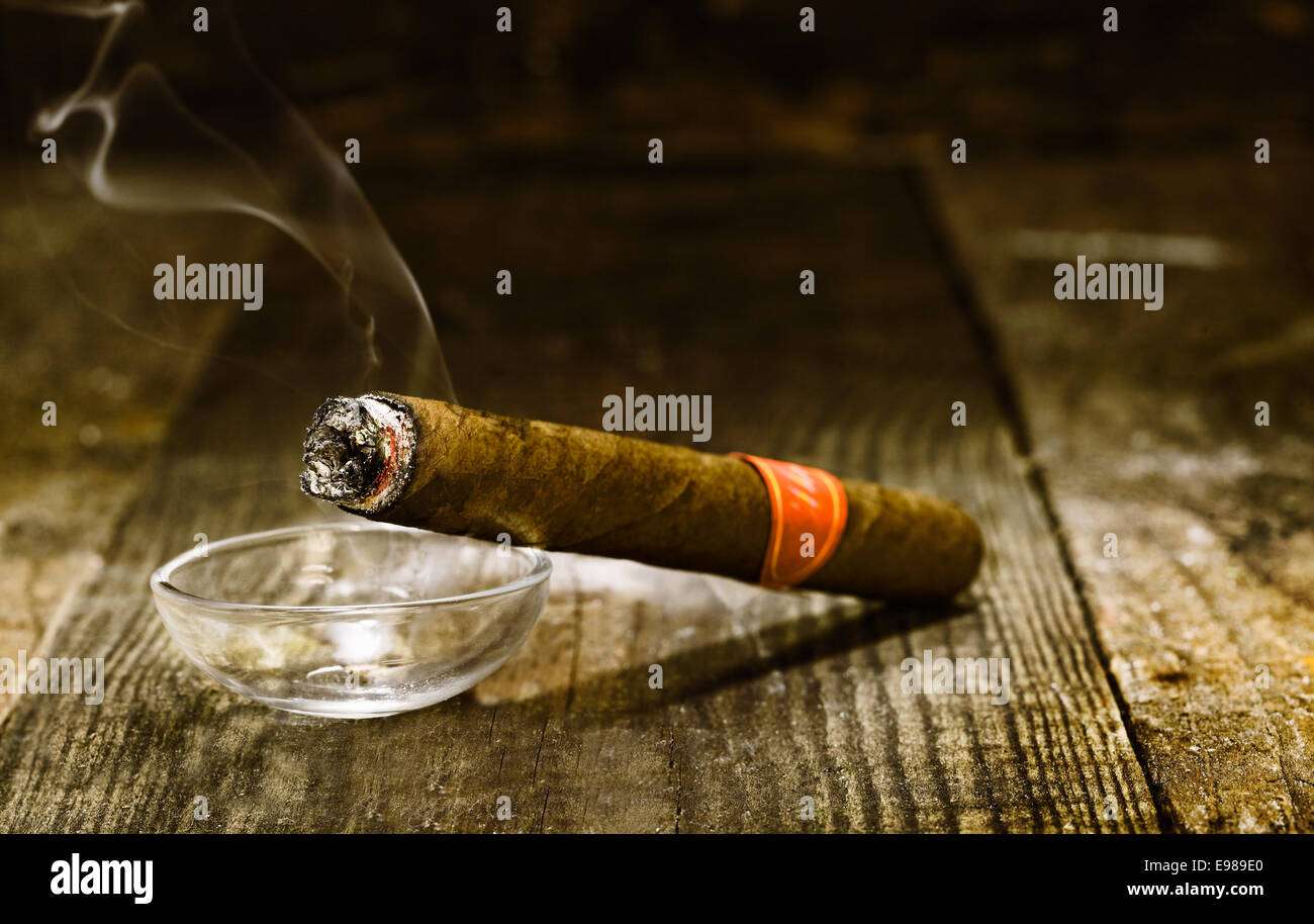 Masterizzazione di lusso fatti a mano sigaro cubano in appoggio su un posacenere su un vecchio bancone in legno in una discoteca o bar con copyspace Foto Stock