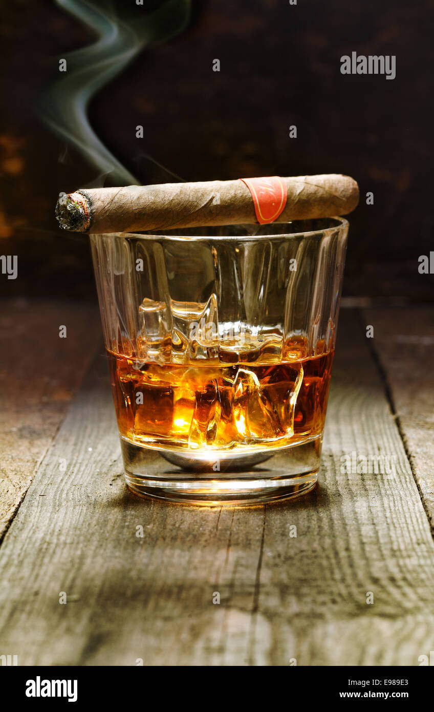 La masterizzazione di sigaro cubano in appoggio su di un bicchiere di brandy in un bar, il lusso piaceri di un facoltoso uomo macho Foto Stock