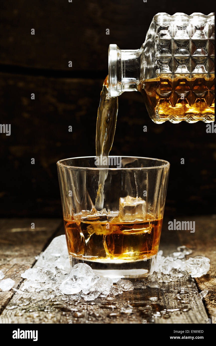 Versando il whisky o Scotch dalla caraffa in vetro con cubetti di ghiaccio Foto Stock