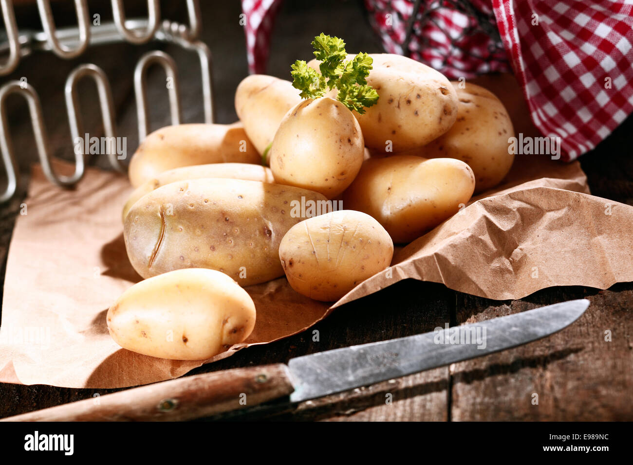 Preparazione di un mucchio di fresco intero di patate su un foglio di carta marrone con un coltello da cucina e trituratore Foto Stock