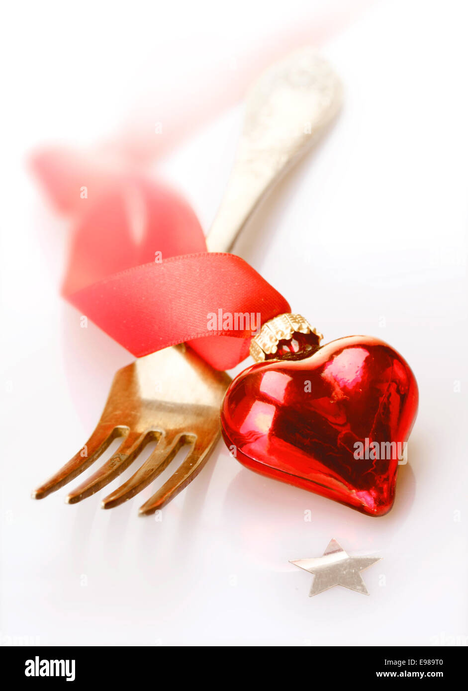 Romantico cuore rosso decorazione con nastro twirled giacendo attraverso una forcella in un Natale, Valentines, matrimonio o anniversario sfondo Foto Stock