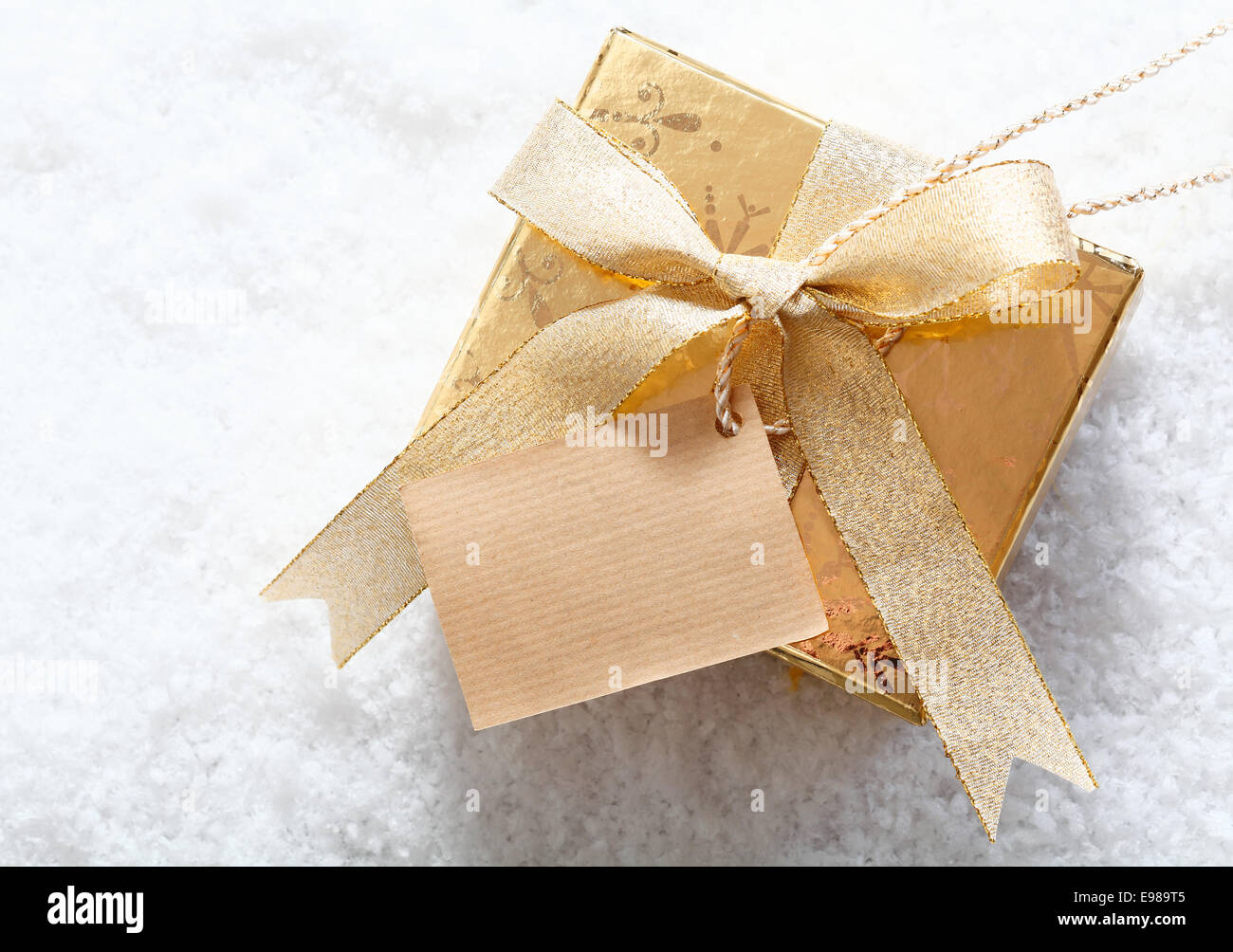 Gold confezione regalo in piedi nella neve con un grazioso inchino e un tag vuoto per la vostra festosa di auguri di Natale Foto Stock