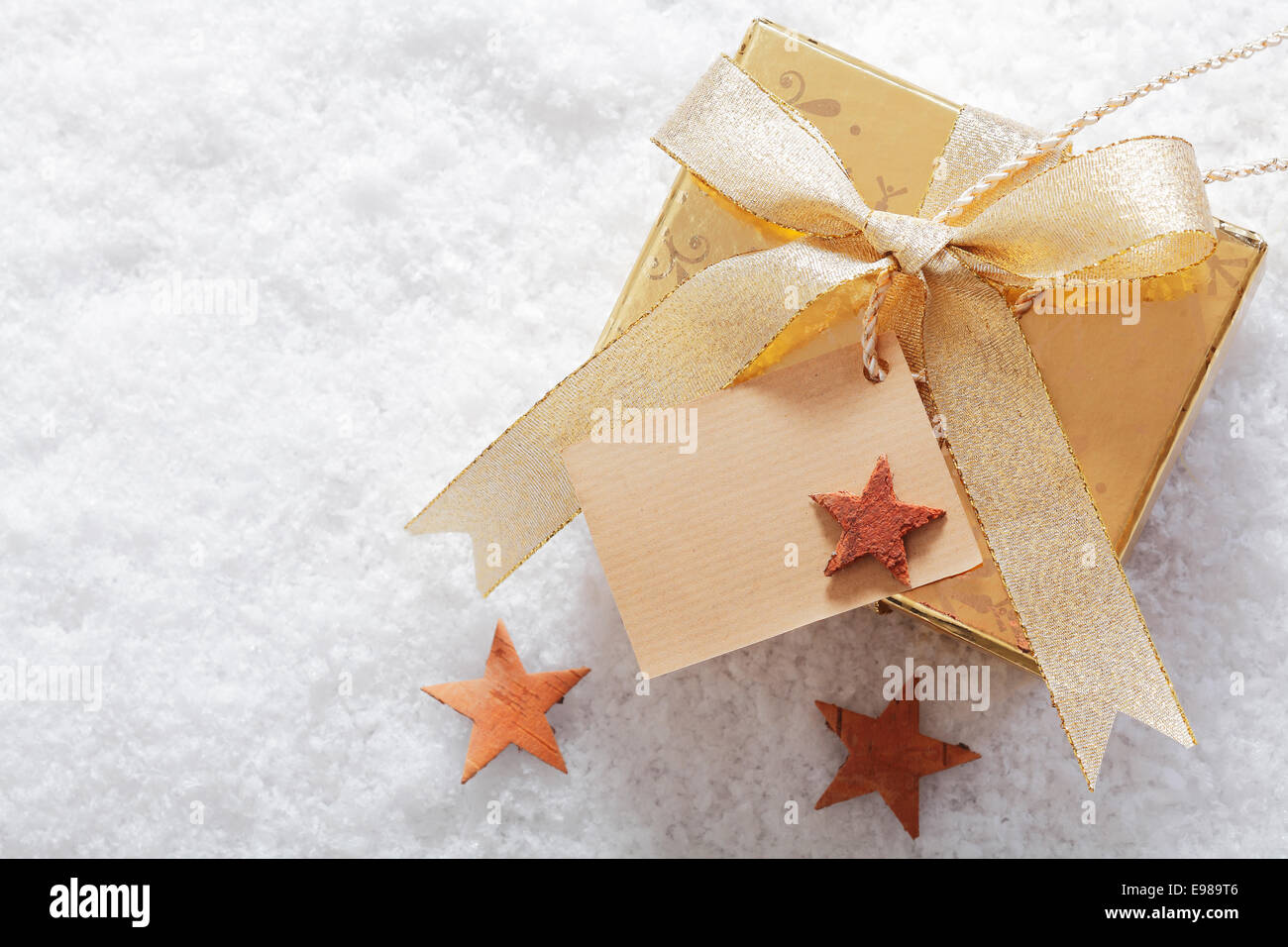 Oro decorativi regalo di Natale in inverno la neve con un'etichetta vuota per il messaggio di saluto stagionali e una dispersione di piccole stelle Foto Stock