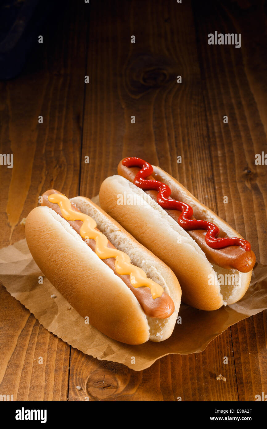 Due hotdog, uno con ketchup, uno con senape su sfondo di legno Foto Stock