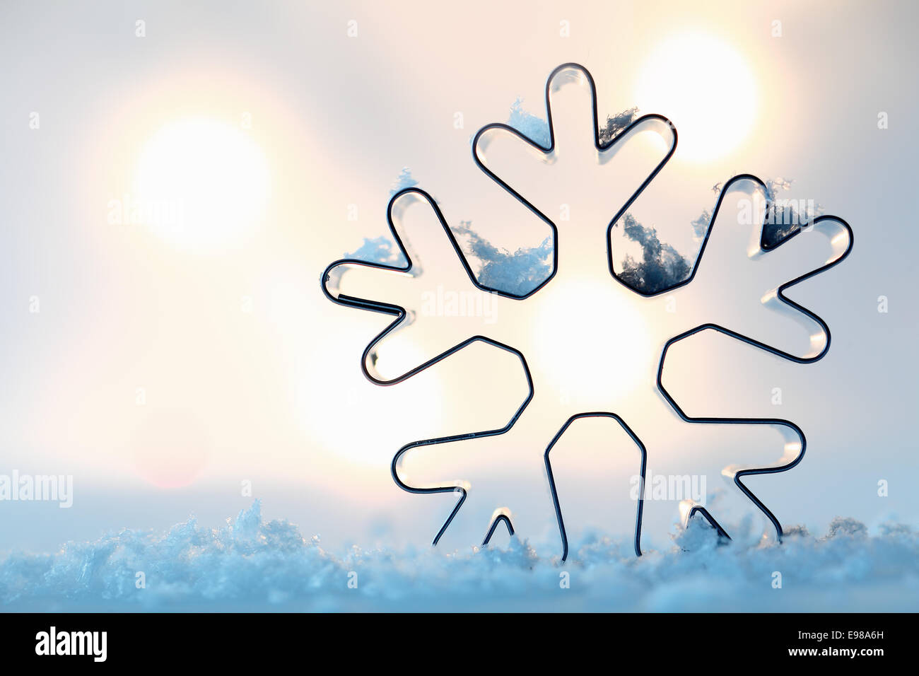 Il contorno di un fiocco di neve in metallo formina su un letto di neve blu con un bokeh di luci incandescenti e copyspace per i vostri auguri di Natale Foto Stock