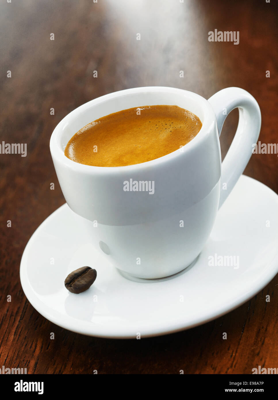 Una completa bianca tazza di caffè con un solo chicco di caffè sul piattino, al buio su un sfondo di legno Foto Stock
