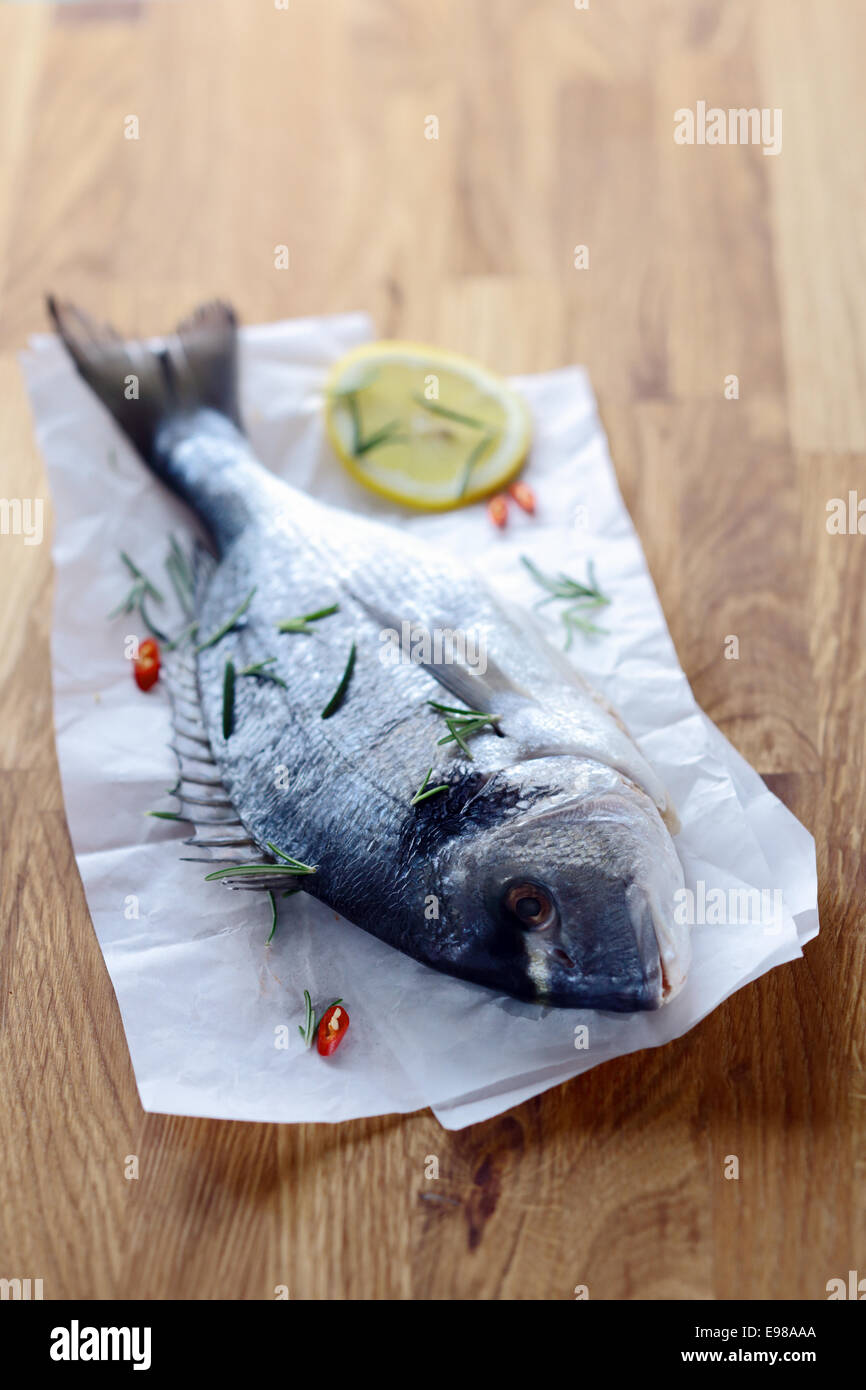 Tutto il pesce crudo su carta sgualcita giacente su una cucina in legno il tavolo è in attesa di essere raccordate per cucinare come una piacevole cena a base di pesce Foto Stock