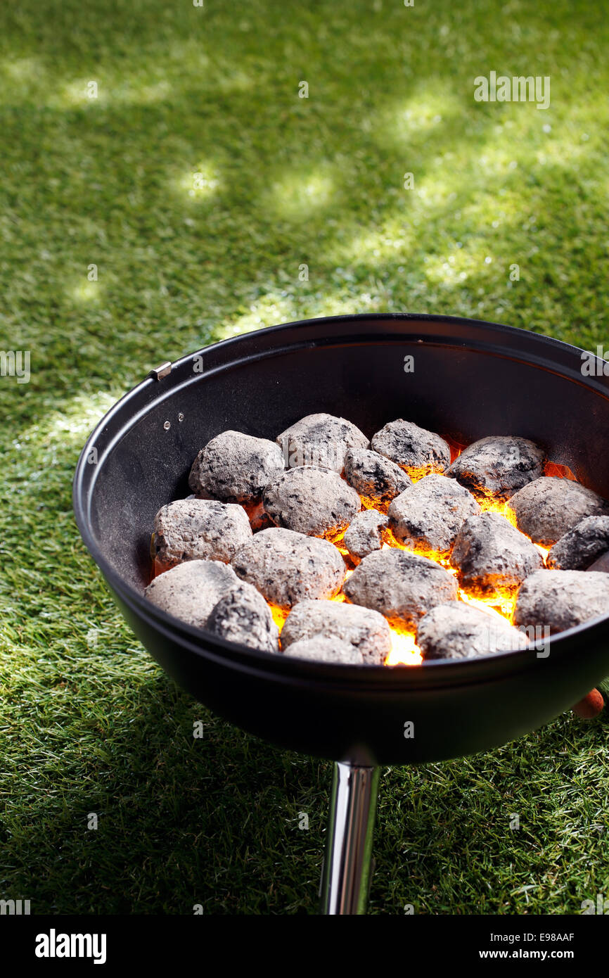 Angolo di alta vista di incandescente braci di carbone in un piccolo barbecue portatile in piedi su erba in preparazione per la cottura di un sano pasto all'aperto Foto Stock
