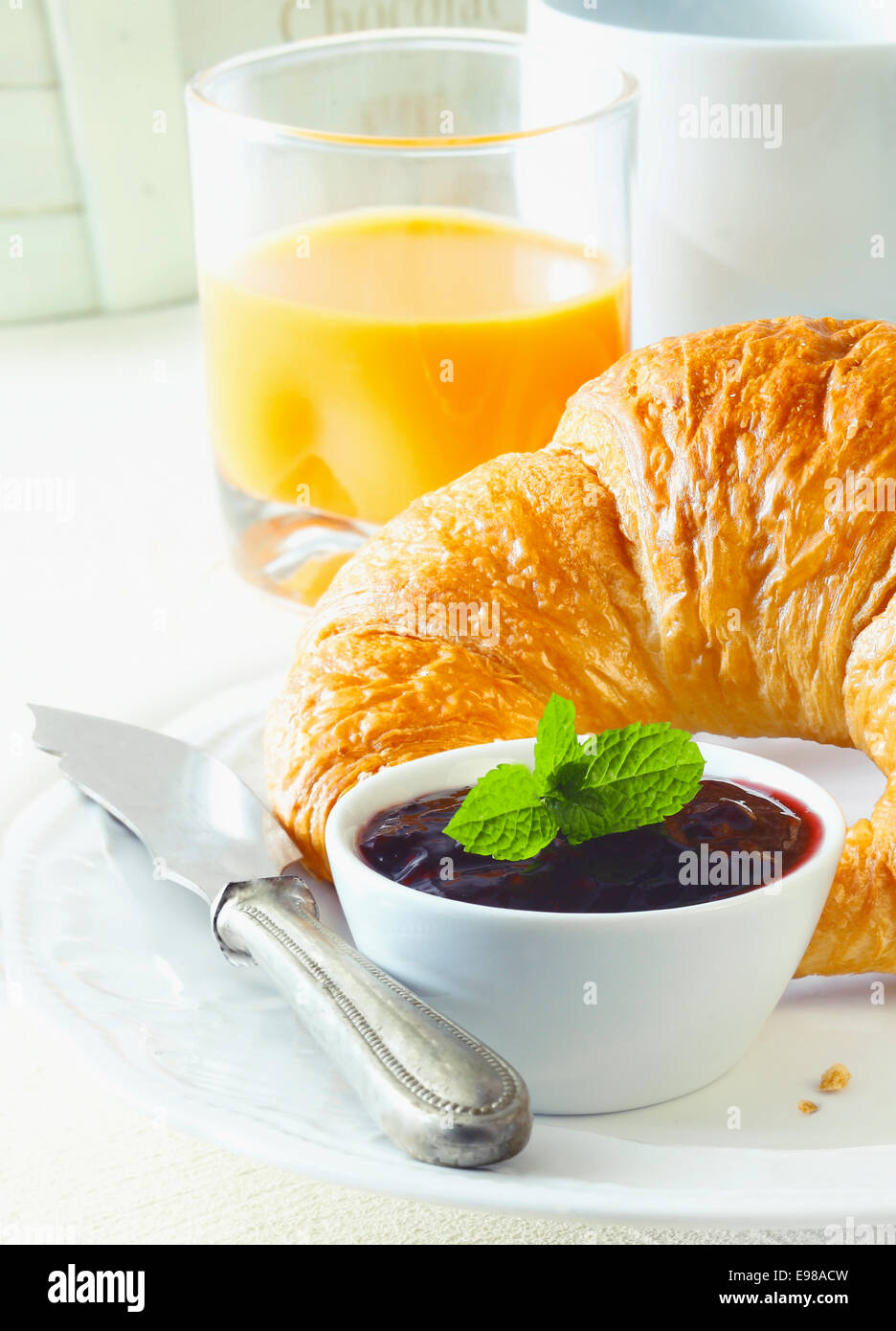 Una sana prima colazione continentale con pane appena sfornato fresco burroso croissant e un vasetto di marmellata accompagnata da un bicchiere di succo d'arancia fresco Foto Stock