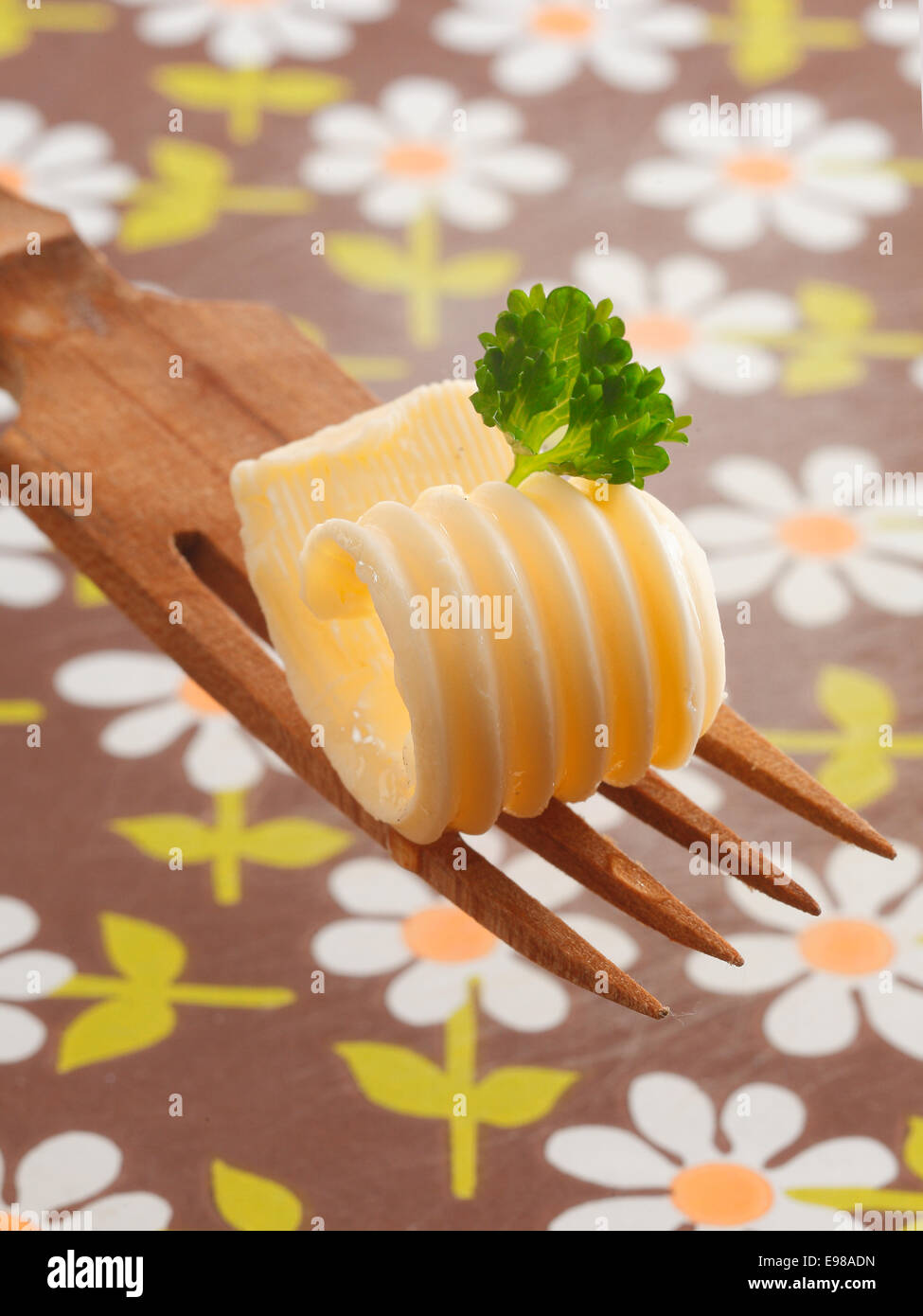 Arricciatura decorativa di laminati di burro o margarina guarnito con menta fresca offerti su una insalata in legno forcella con una tovaglia di floral background Foto Stock
