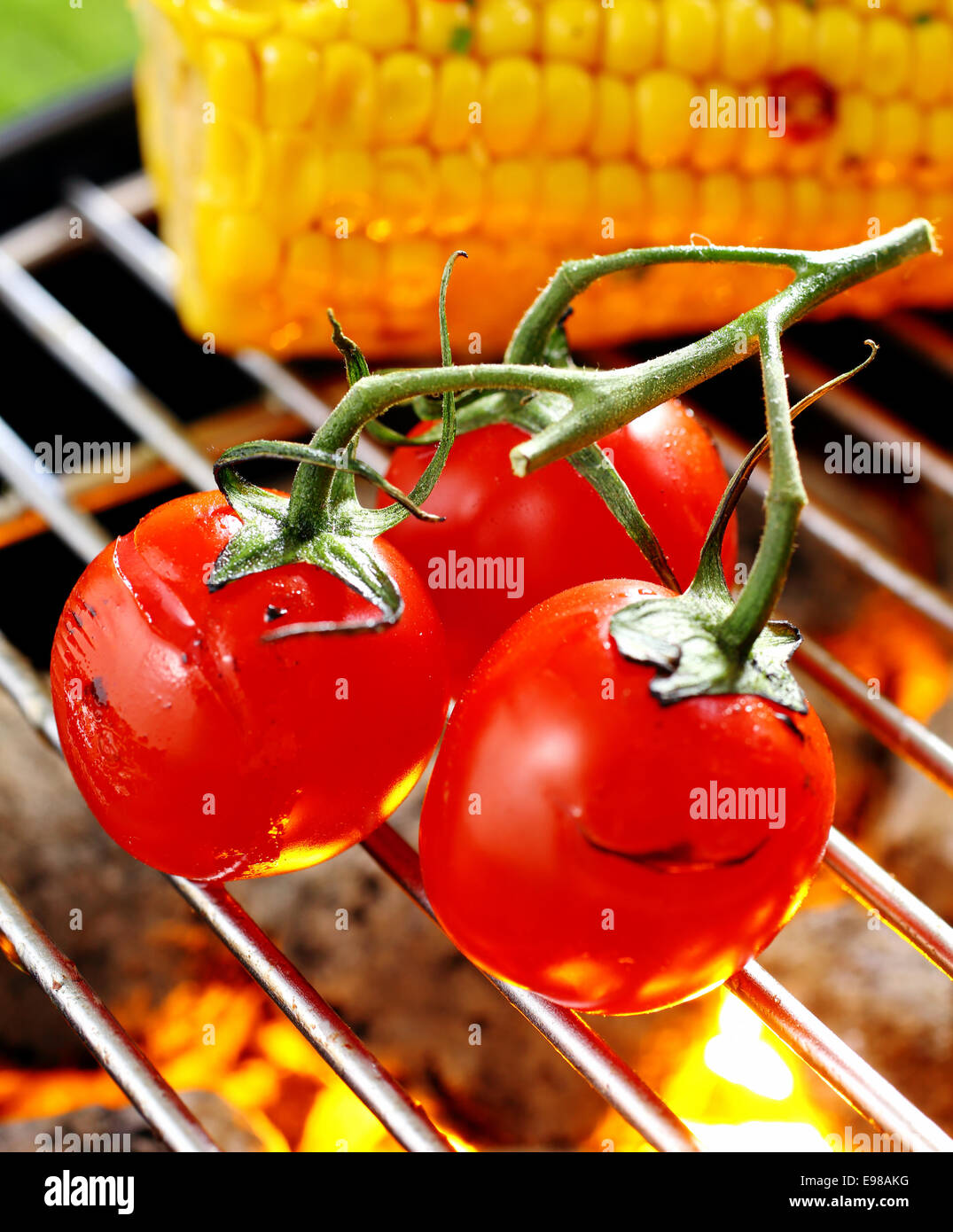 Tre maturi rossi pomodori ciliegini ancora attaccato alla vite equilibrata su un barbecue grill griglia su un fuoco Foto Stock