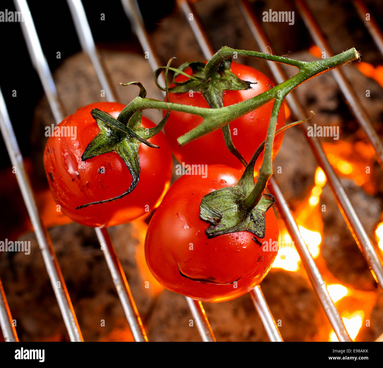 Mazzetto di ripe rosso pomodori ciliegia sulla vite tostatura su un barbecue fire, ad alto angolo di visione della griglia e carbone incandescente Foto Stock