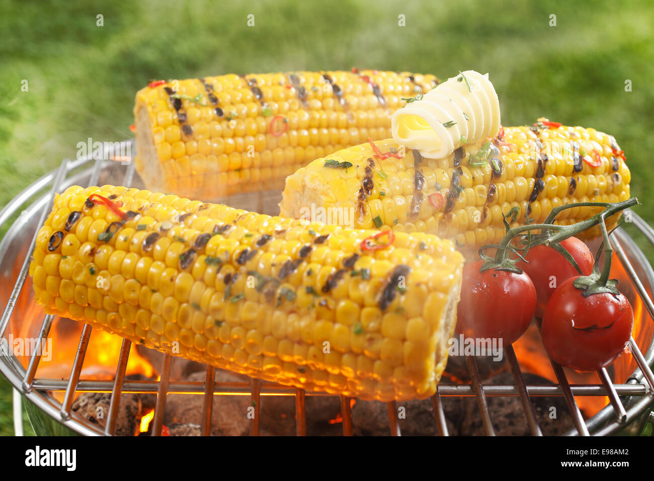 Un sano barbecue vegetariano con maturi golden sulla pannocchia di mais e succosa rossi pomodori ciliegini grigliare sul fuoco all'aperto su un Foto Stock