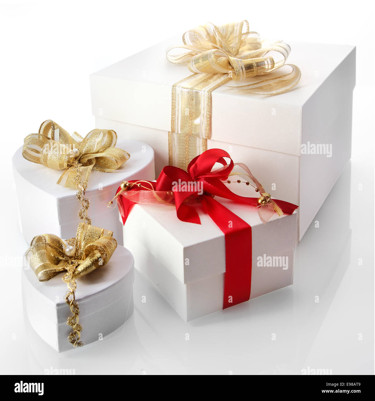 Raccolta di bianco doni decorativi inclusi cuore cassetti sagomati con eleganti nastri oro legato con treccia e perle su un bianco riflettente sfondo per celebrare il Natale, San Valentino, un compleanno o un anniversario Foto Stock