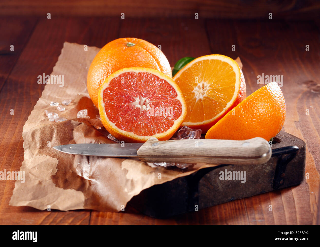 Succose arance, uno insieme e alcuni tagliate a metà su carta marrone con coltello Foto Stock