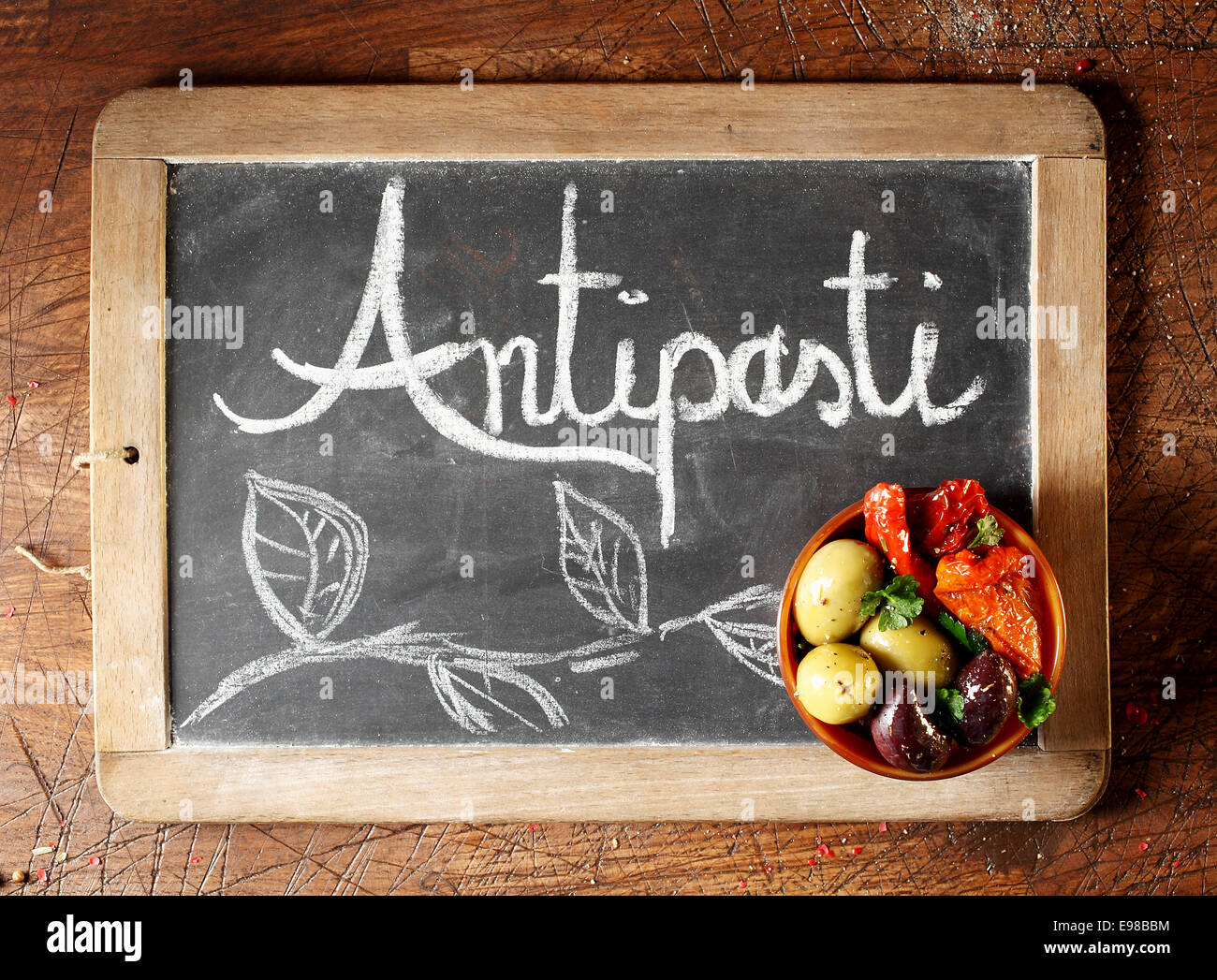 Chalkboard Antipasti a firmare con il testo scritto a mano e il fogliame decorativo con una piccola ciotola di olive nere e verdi e peperoncino nell'angolo, vista aerea su un sfondo di legno Foto Stock