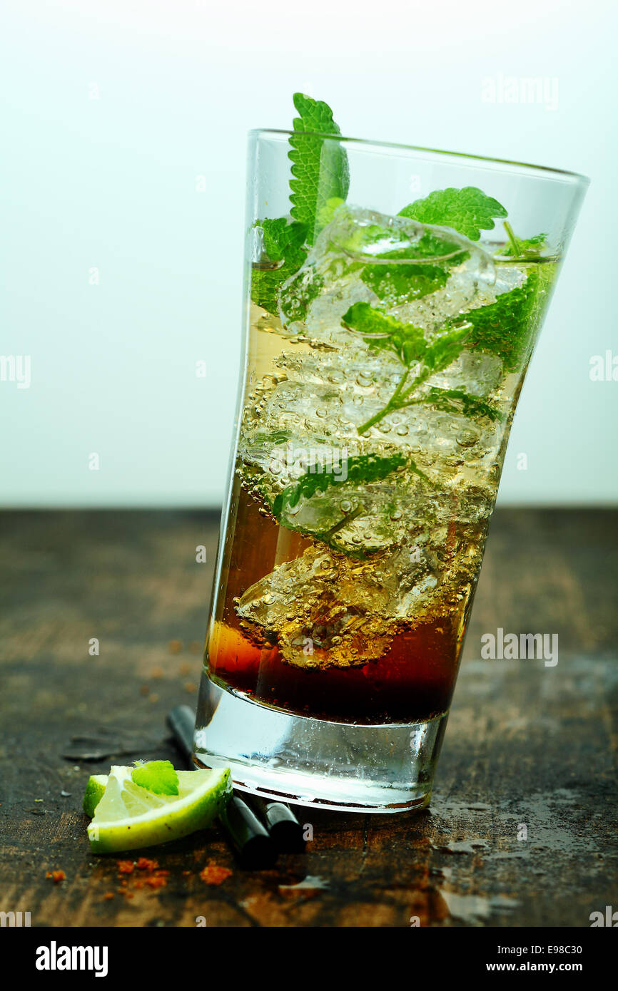 Iced cocktail mojito con il rum e menta servito in un bicchiere alto su un vecchio tavolo di legno o banco bar Foto Stock