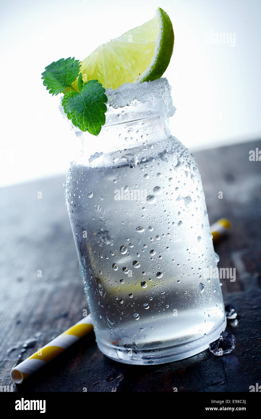 Vaso di ghiaccio su un tavolo di legno con un cuneo di lime e foglie di menta. Guarda il mio portfolio per ulteriori cocktail. Foto Stock