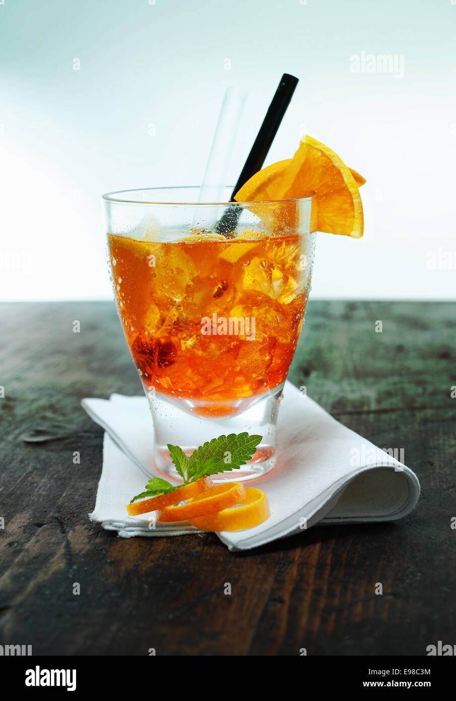 Servire di aperol spritz cocktail con ghiaccio guarnite con foglioline di menta e la scorza di arancia su un tovagliolo piegato su un vecchio banco di legno in un bar o club Foto Stock