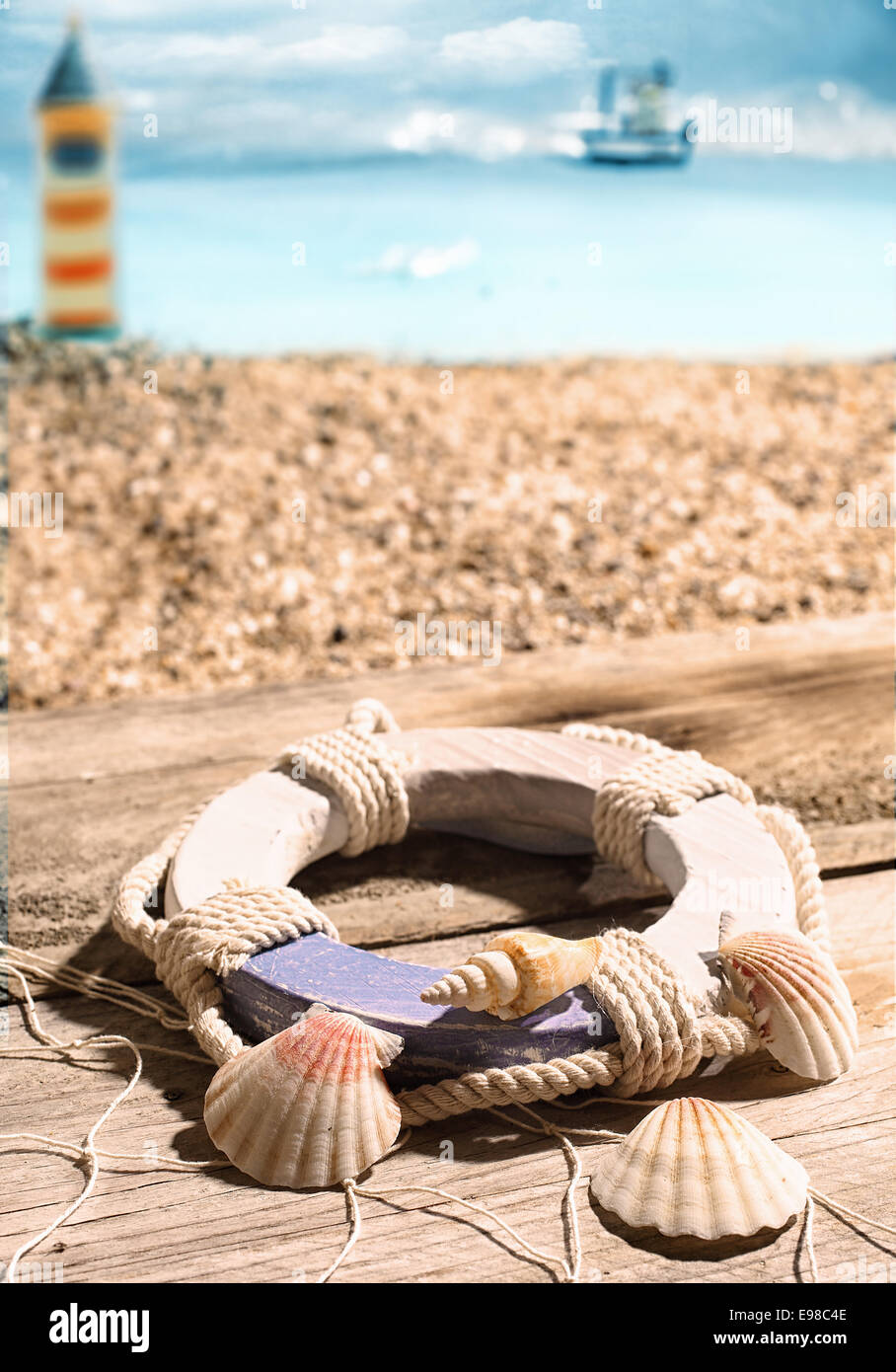 Anello di vita e conchiglie giacente su vecchie tavole di legno drappeggiate in un pesce net che si affaccia sulla spiaggia e sulla costa con un faro a distanza Foto Stock