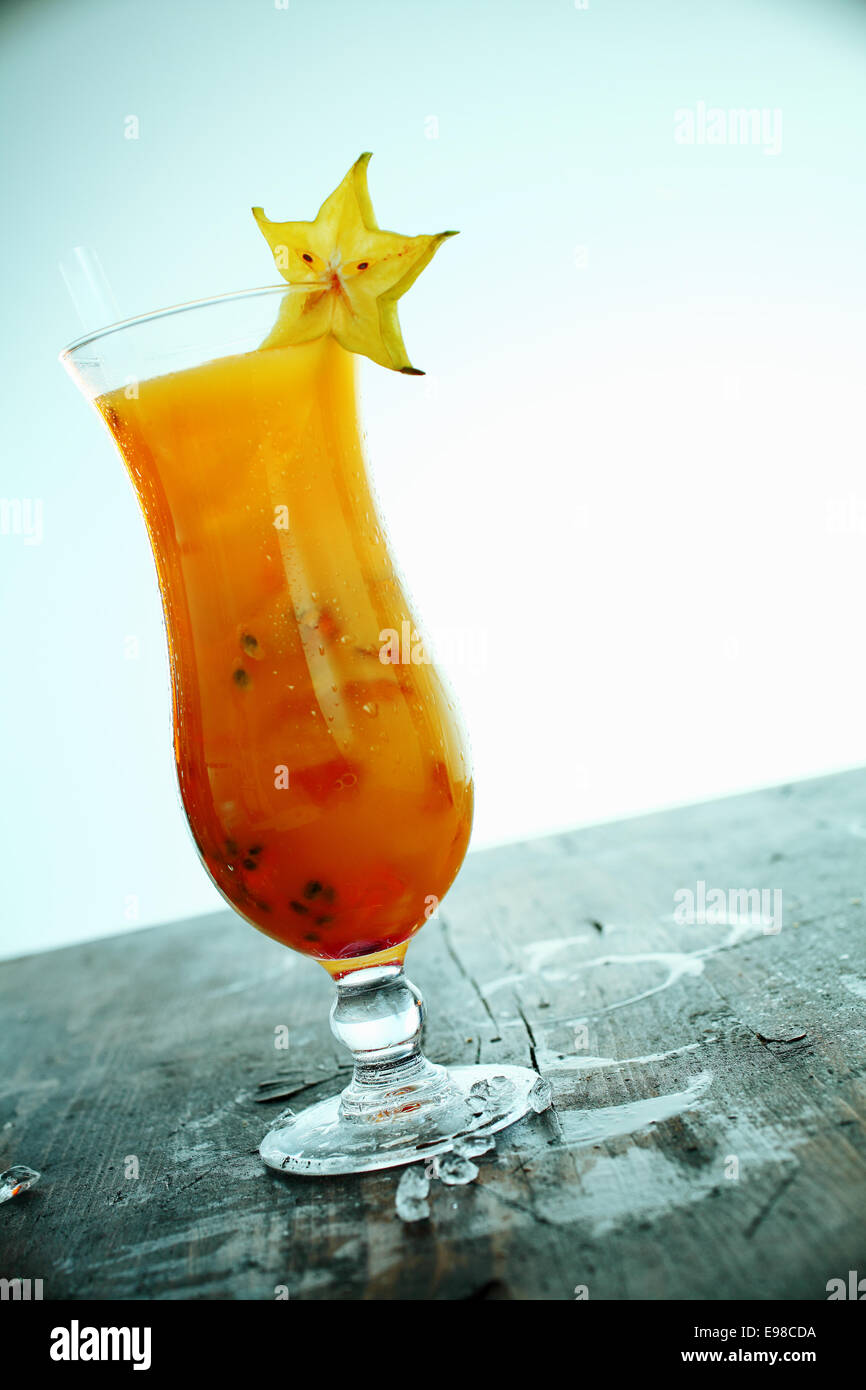 Esotici e coloratissimi orange carambole cocktail a base di frutta e ghiaccio servita in un bicchiere a lungo su un vecchio bar in legno contatore con fuoriuscite Foto Stock