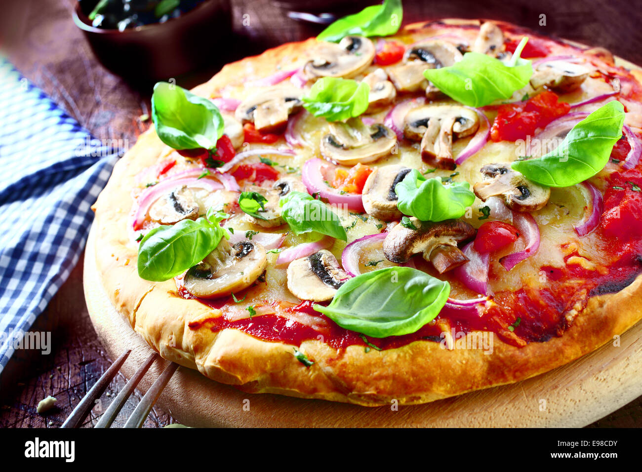 Una deliziosa pizza vegetariana condito con pomodoro, formaggio fuso, funghi, cipolle e di foglie di basilico fresco servito su una tavola di legno, ad alto angolo di visione. Più la pizza alla mia porta. Foto Stock