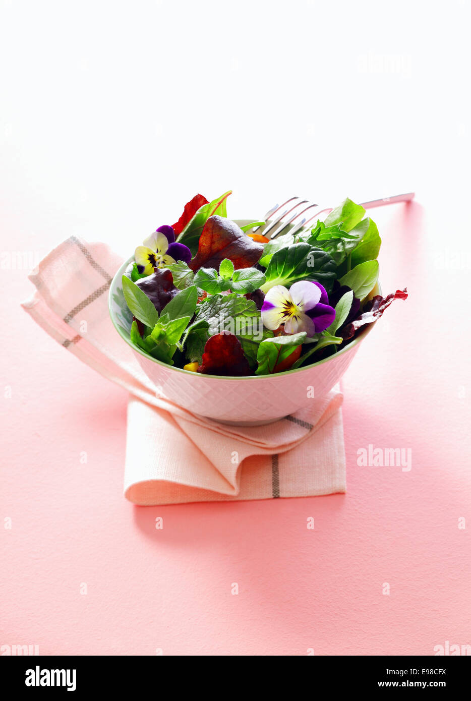 Singoli che serve di erba fresca insalata con i Nasturzi fiori in un vaso di porcellana è servita come accompagnamento per un pasto su un tavolo bianco igienico Foto Stock