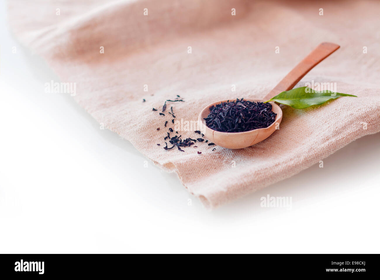 Shredded essiccato loose-foglia di tè per preparare una deliziosa tazza di fresco di bevanda calda visualizzata su un piccolo cucchiaio di legno su un tovagliolo piegato con copyspace Foto Stock