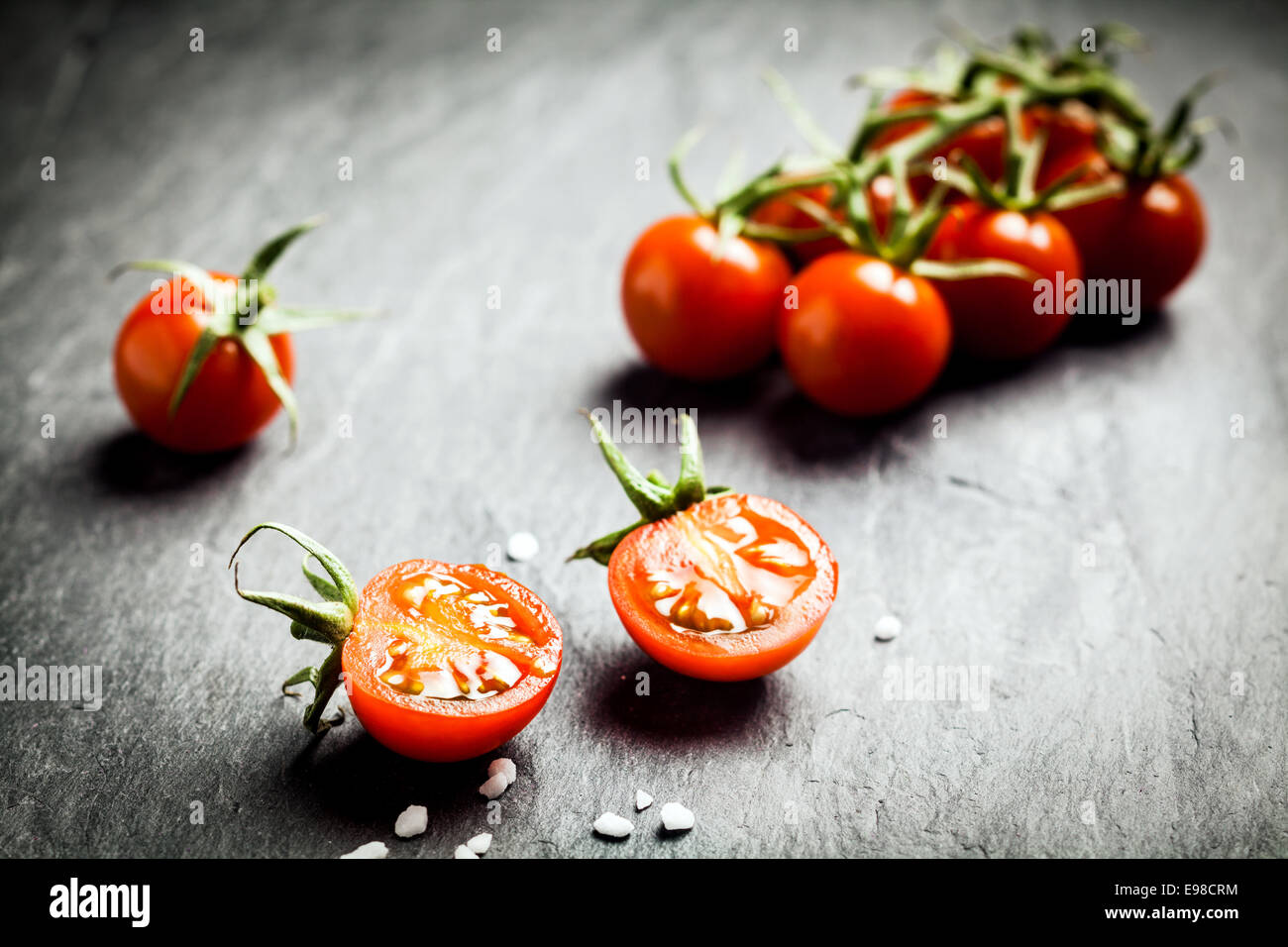 Dimezzato fresche e mature di pomodoro di uva che mostra i punti di interfacciamento di chiazza e succosa polpa in primo piano con un mucchio di pomodori sulla vite dietro su Foto Stock