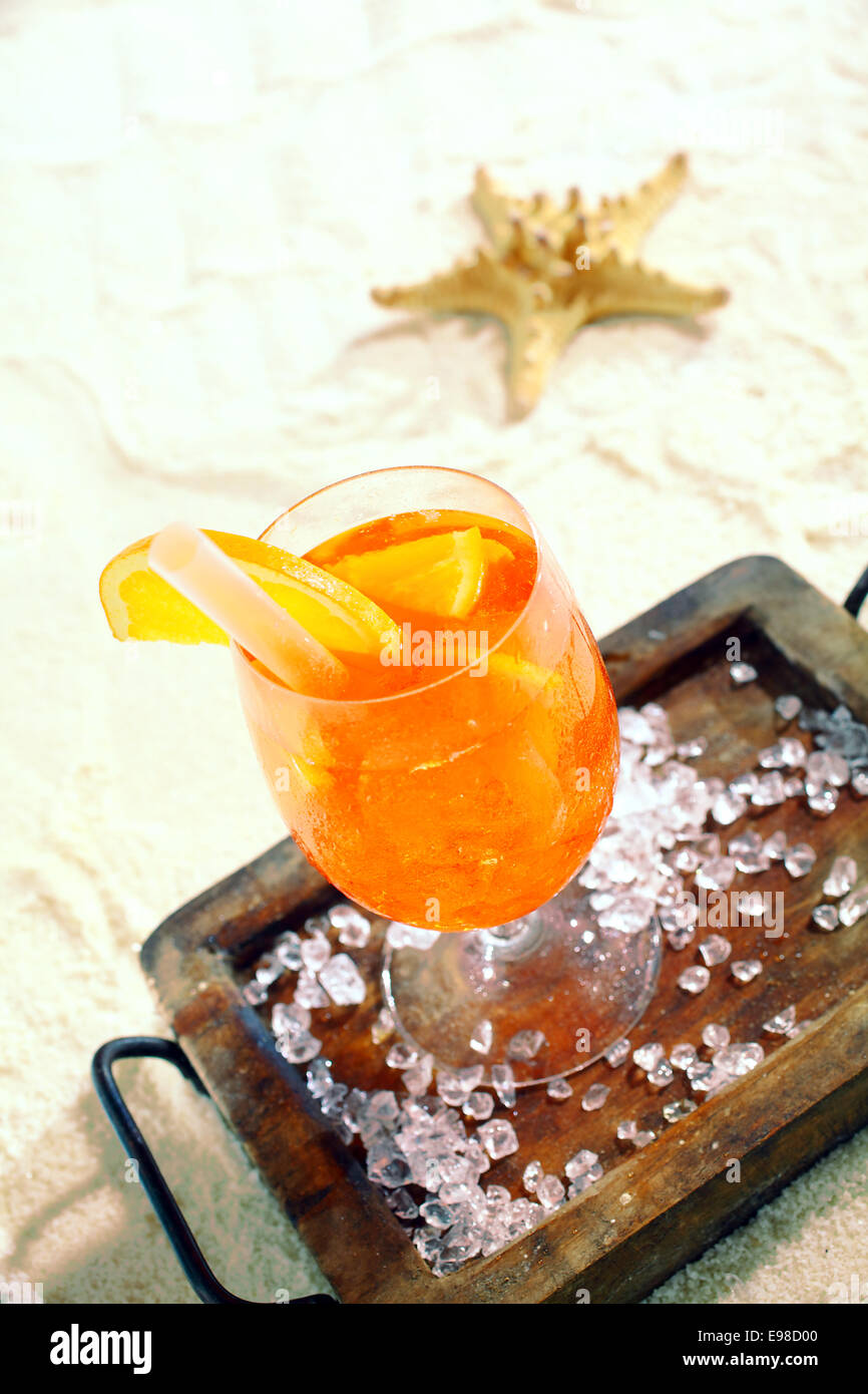 Daiquiri alla arancione e cocktail di agrumi in piedi su un vassoio di legno su una spiaggia tropicale con una stella di mare in background Foto Stock