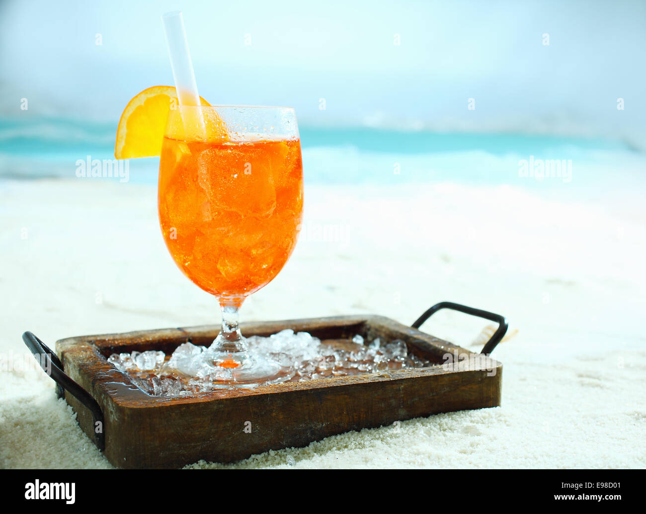 Tropical arancione e il daiquiri alla cocktail in piedi su un vassoio di legno con ghiaccio tritato su una spiaggia assolata su una vacanza estiva Foto Stock