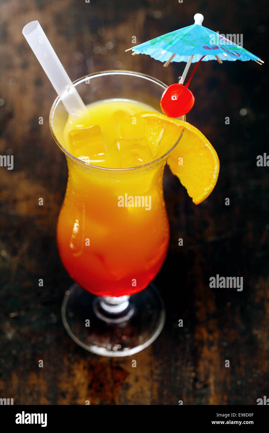 Elevato angolo di visione di un bicchiere di orange daiquiri cocktail serviti con una cannuccia e guarnito con una ciliegia di colore rosso su un cocktail ombrello per una festosa celebrazione di partito Foto Stock