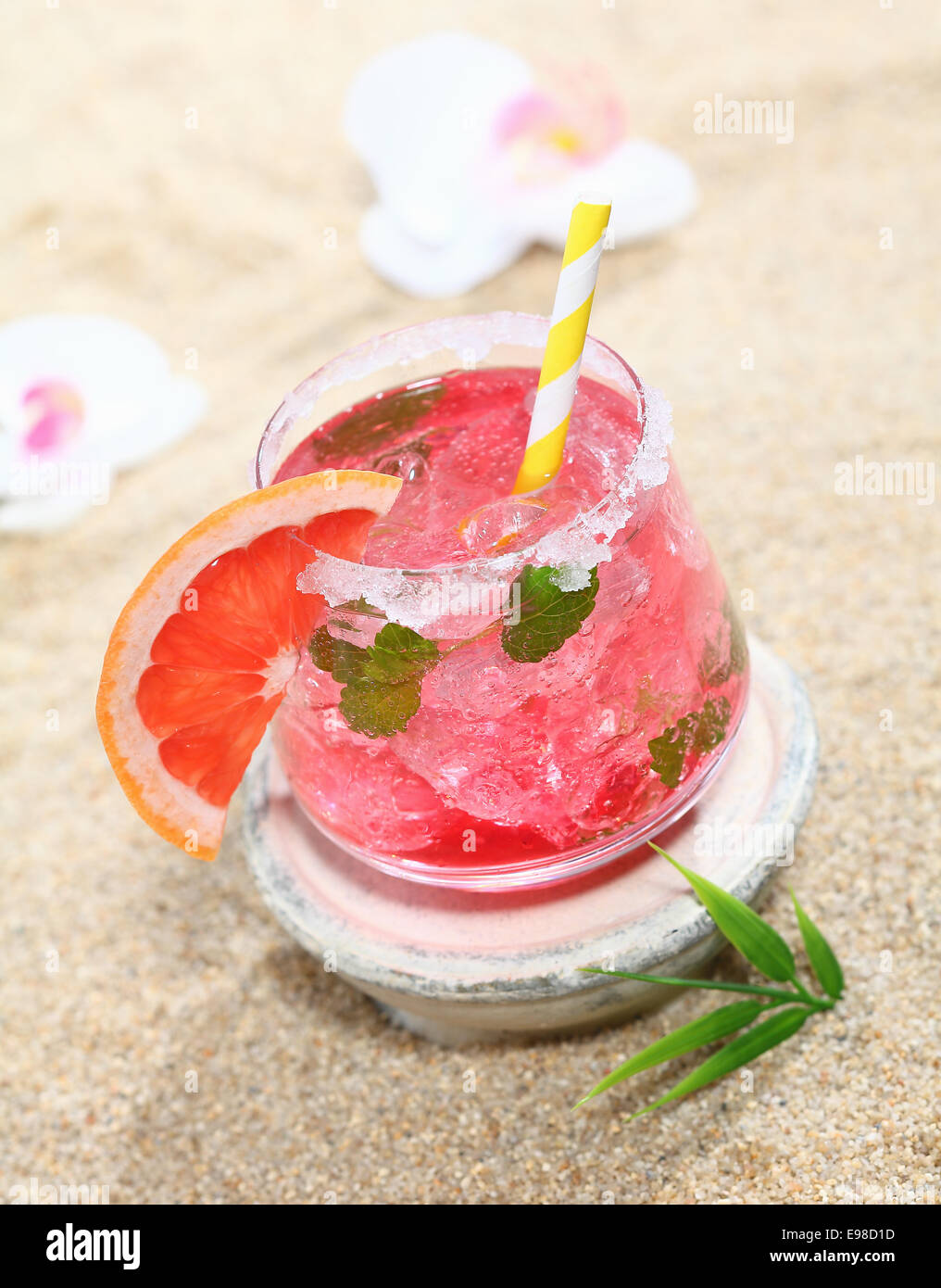 Angolo di alta vista di una deliziosa refrigerate cocktail tropicale sulla spiaggia guarnita con arancia e servite con una cannuccia Foto Stock