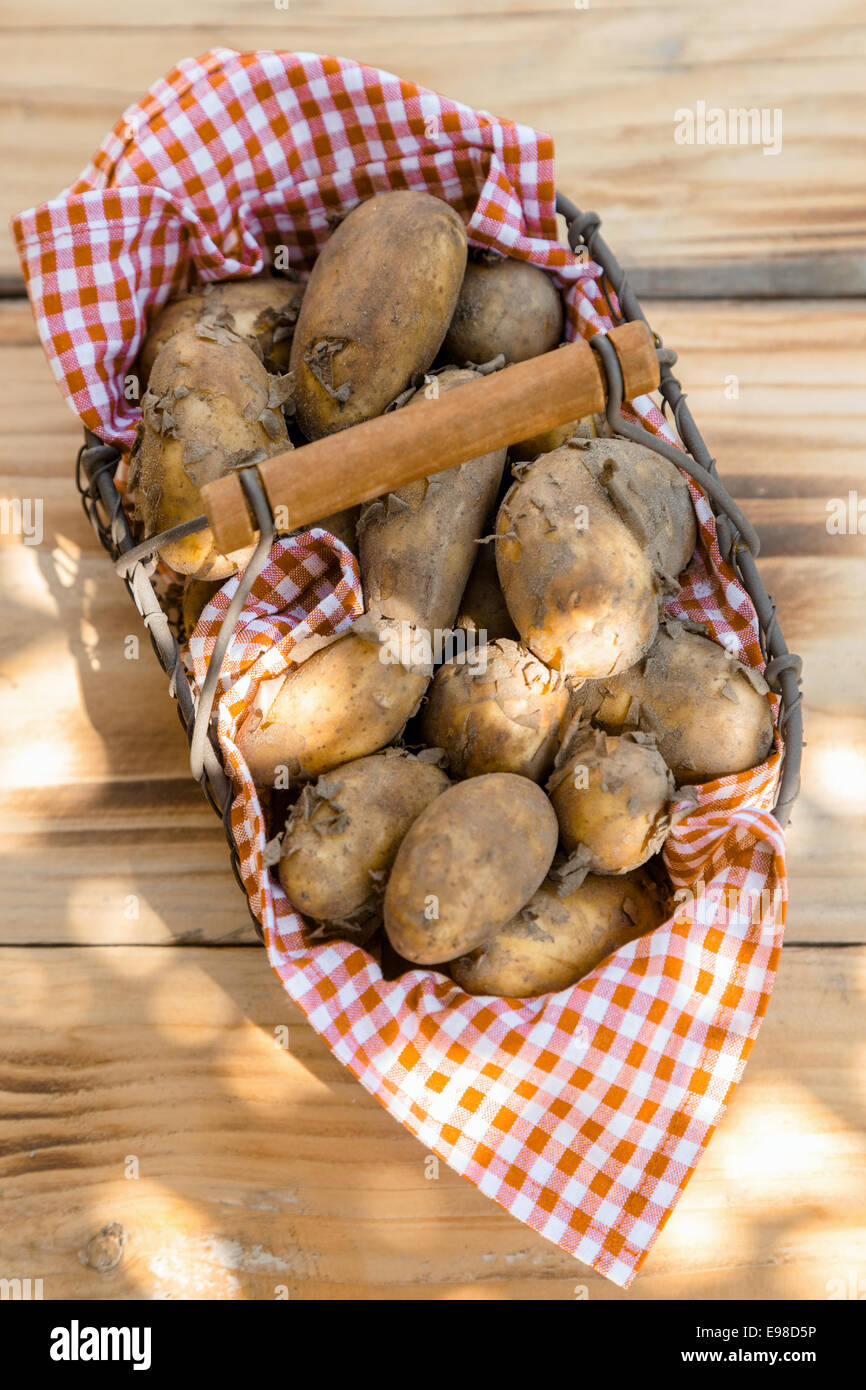 Vista aerea di un cesto in filo di farm Patate fresche in un colorato di rosso e bianco tovagliolo controllato su una tavola di legno al mercato degli agricoltori Foto Stock
