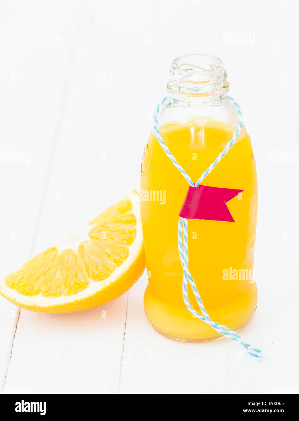 Freschi Fatti in casa tropicale di succo di arancia in una bottiglia di vetro con un tag a fianco di una fetta di arancia fresca che mostra la succosa polpa bianca su tavole di legno Foto Stock