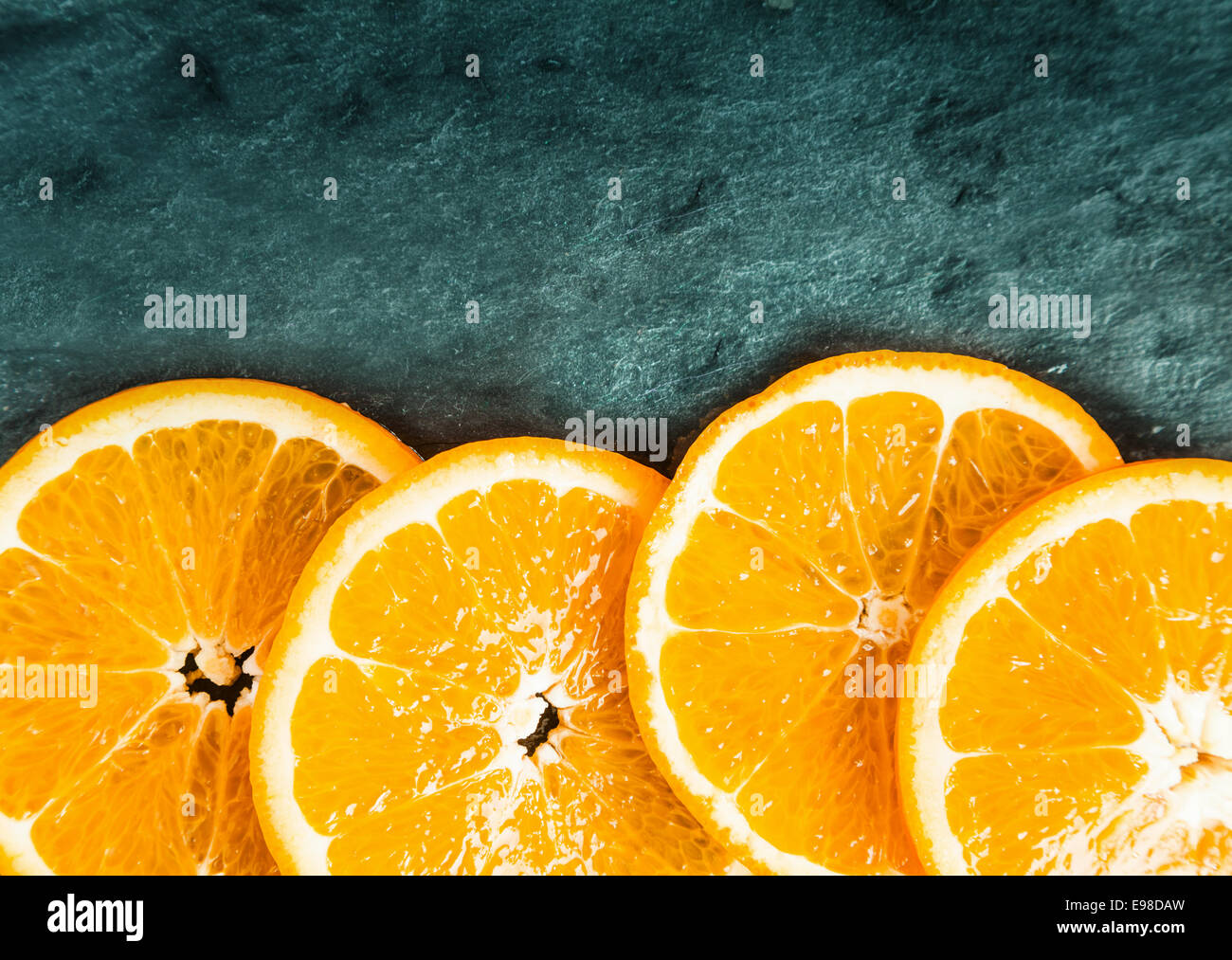 Colorate fresche succose fette di arancio disposte come un confine inferiore su ardesia testurizzata con angolo superiore vignettatura e copyspace Foto Stock
