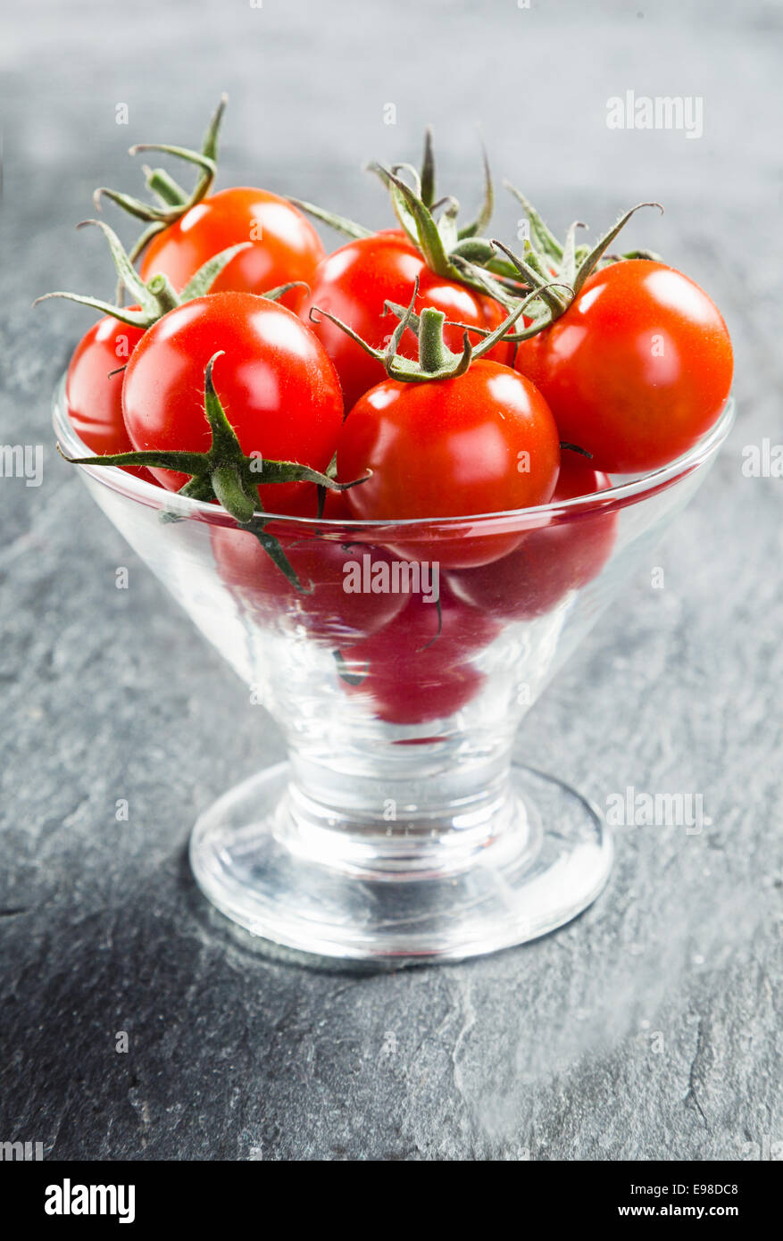 Fresche e mature red succosi pomodorini con piccioli servito in un bicchiere conico contenitore come crudites di immergere in una salsa saporita Foto Stock