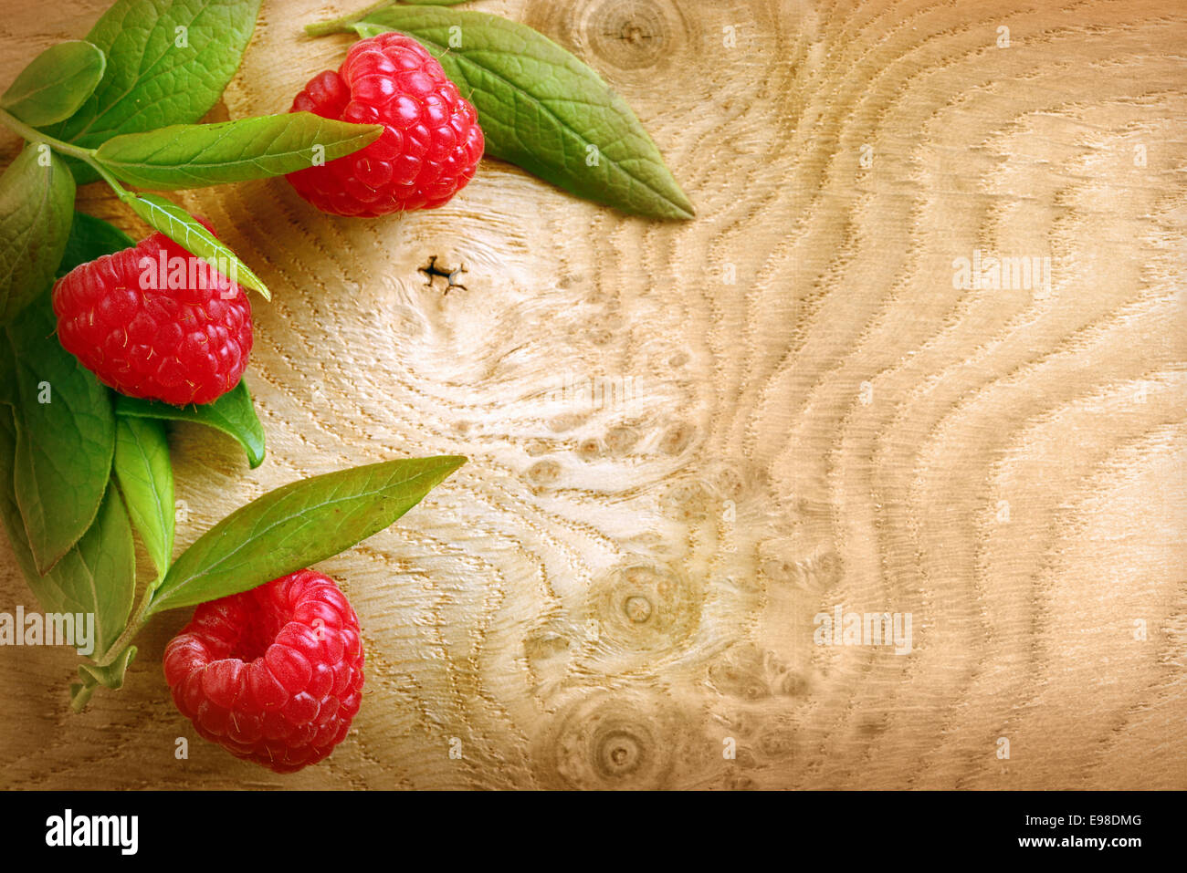 Ripe rosso lampone e foglie su un modellato woodgrain texture con copyspace Foto Stock