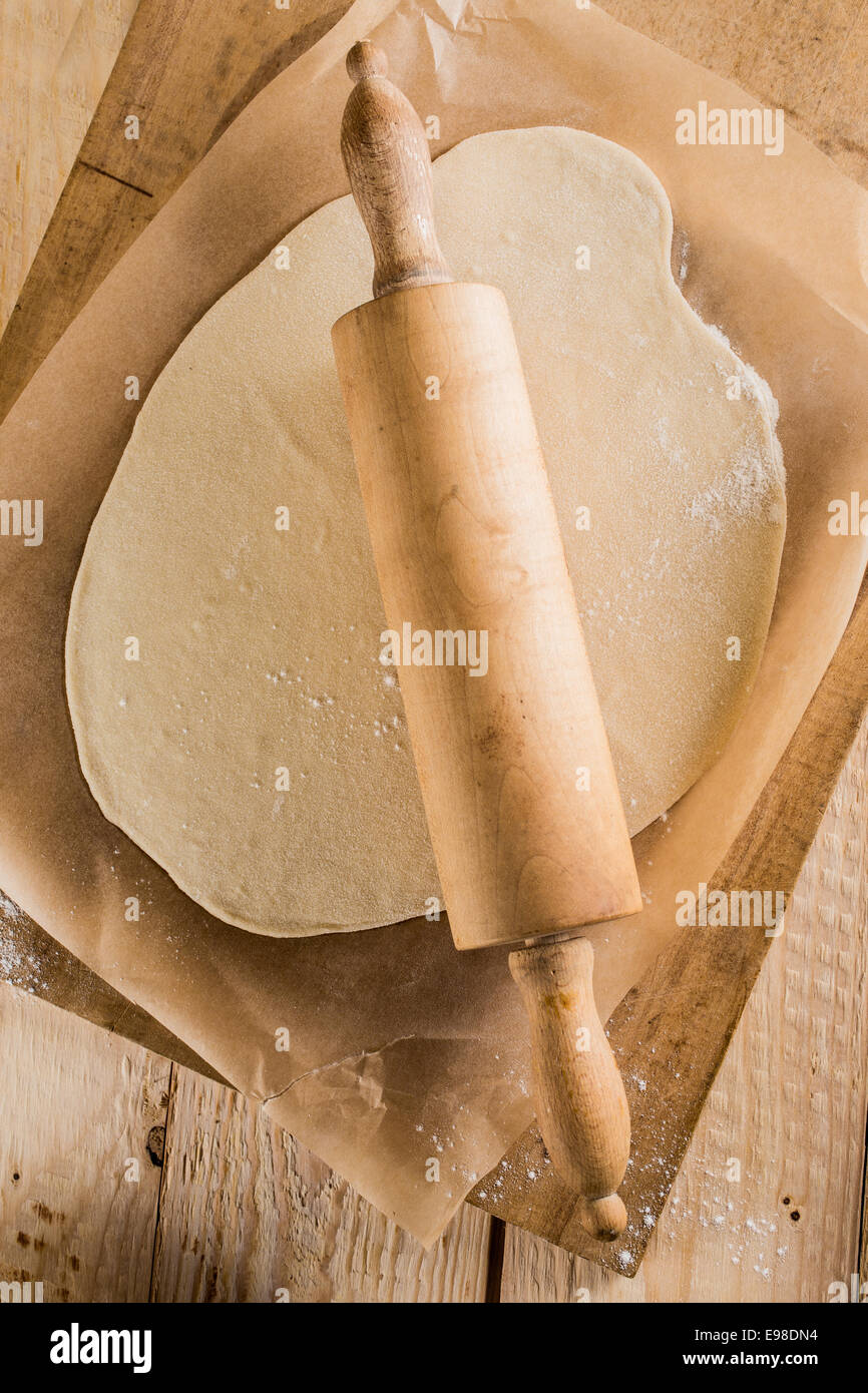 Rendendo la pizza fatta in casa in un paese cucina con una vista aerea di pasta laminata per la base con una laminazione di legno pin su carta forno su un vecchio tagliere di legno Foto Stock