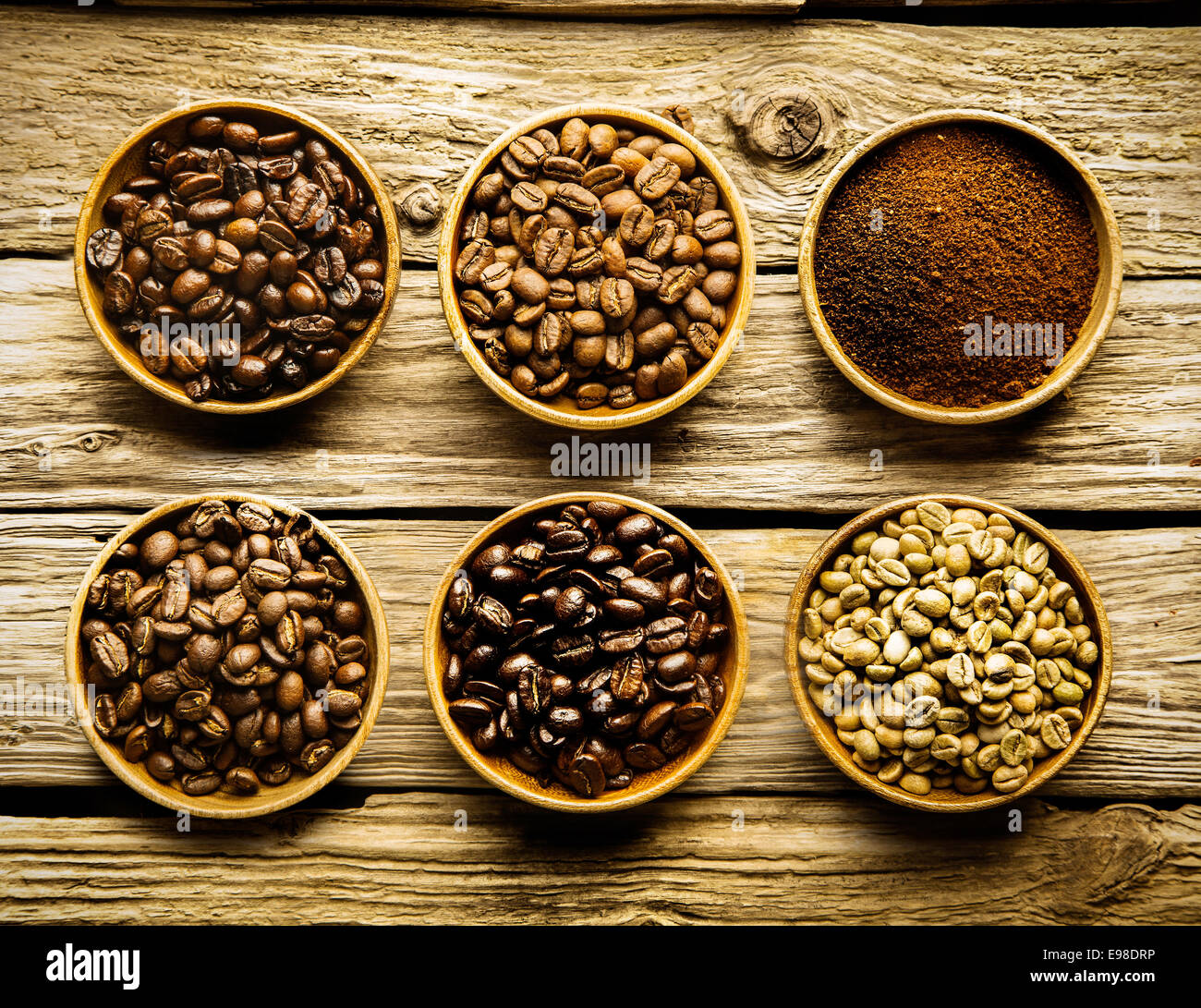 Cinque varietà di caffè in grani e macinato è piatti separati che mostra i diversi punti di forza e di colore dei fagioli di materie attraverso un mezzo a pieno arrosto su un weathered driftwood sfondo Foto Stock