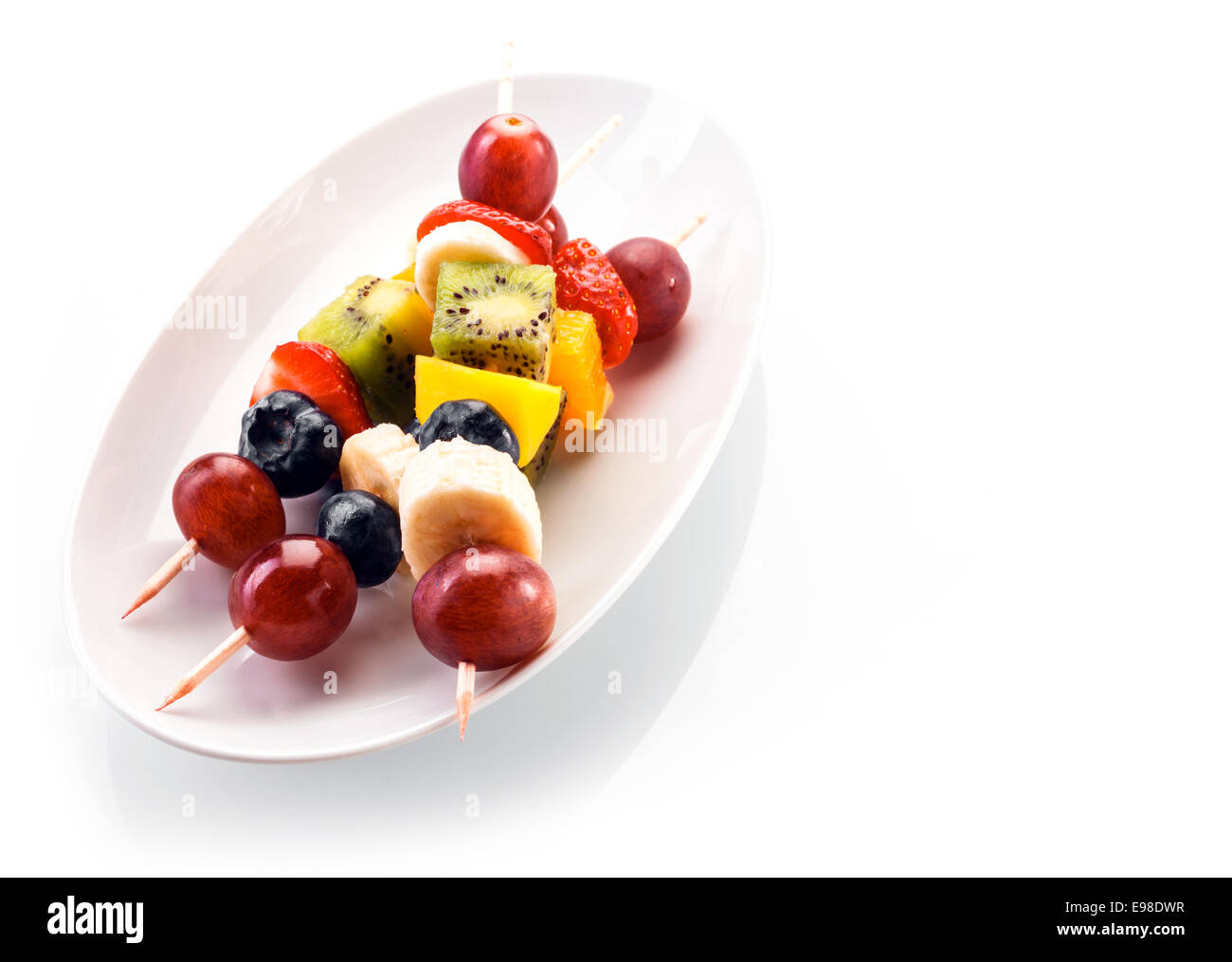 Fresco e salutare la frutta tropicale di spiedini con uve, mirtilli, banana, arancio, kiwi e fragole servite su un ovale bianco Foto Stock