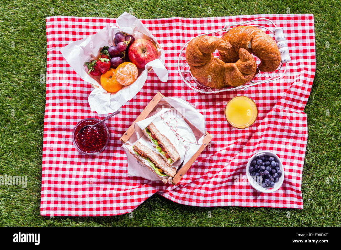Fresco e salutare picnic estivo il pranzo è servito su un rosso e bianco paese controllato il panno con panini, frutta, croissant e arancione Foto Stock