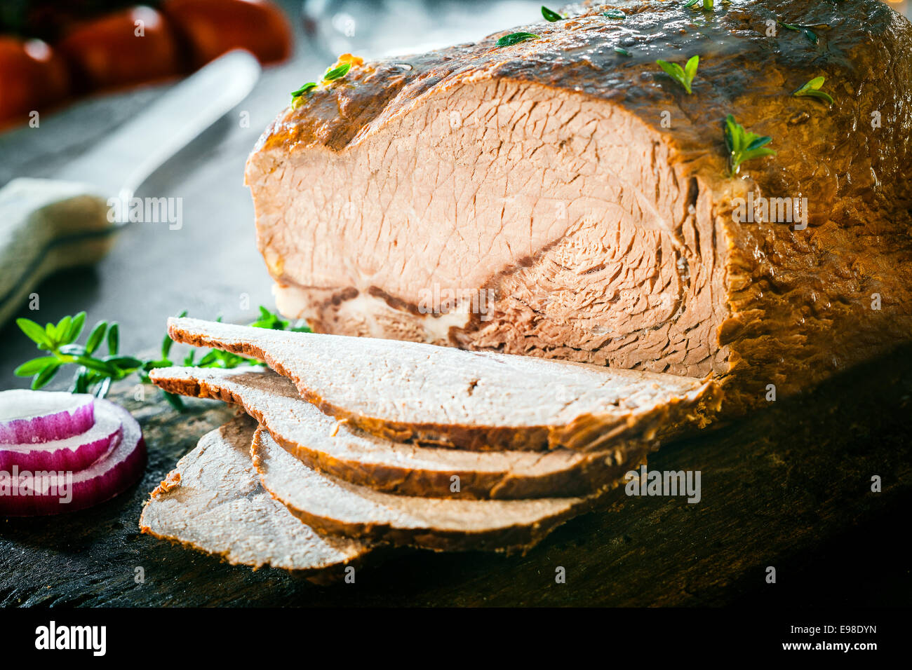 Close up di un gustoso affettato tedesco pagnotta di carne arrostito in una casseruola e condita con erbe fresche su un tagliere di legno Foto Stock