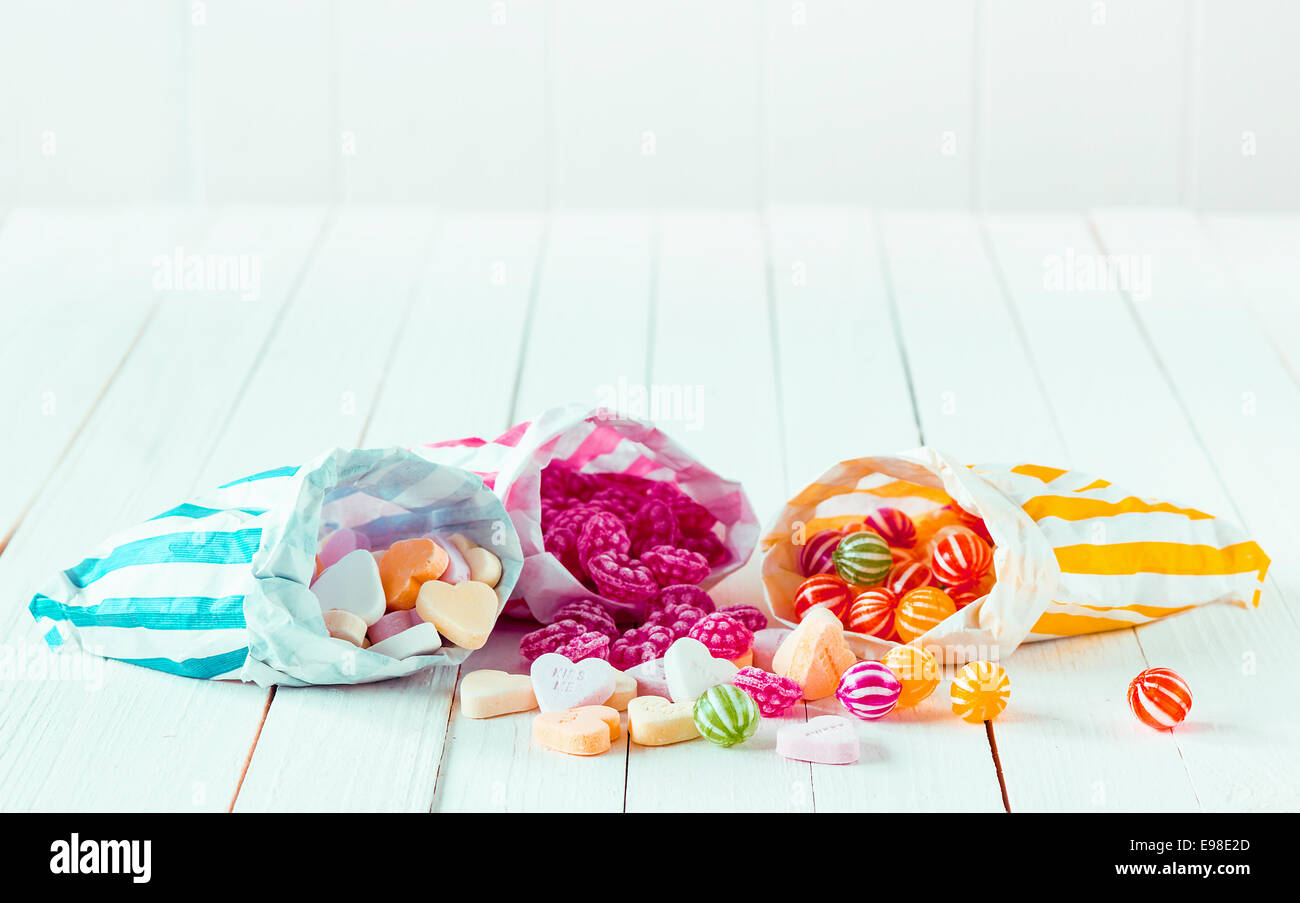 Assortimento di caramelle in tre strisce borse decorate sparsi su un bianco tavolo in legno Foto Stock
