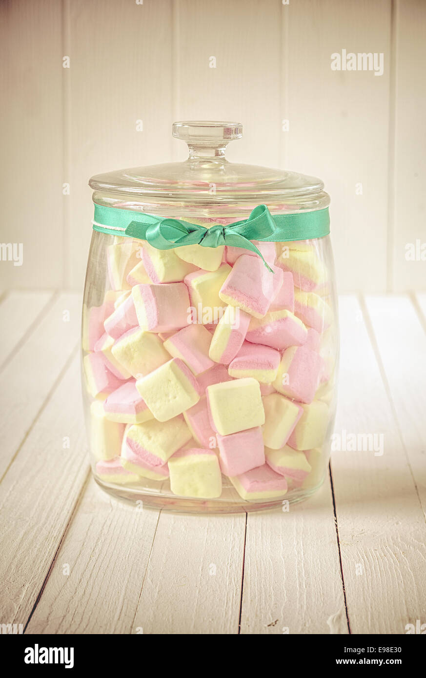 Basso angolo e vista ravvicinata di un vecchio vetro caramelle vaso riempito con quadrato rosa e giallo marshmallows e un nastro di verde su un Foto Stock