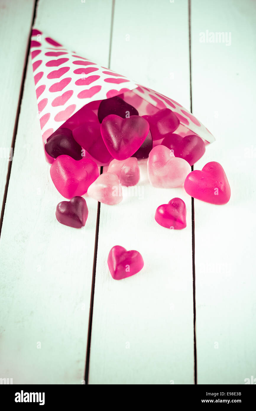 Vista ravvicinata di un cono di caramella decorata con cuori rosa fuoriuscita a forma di cuore ad caramelle gommose oltre un legno bianco bordo tabella Foto Stock