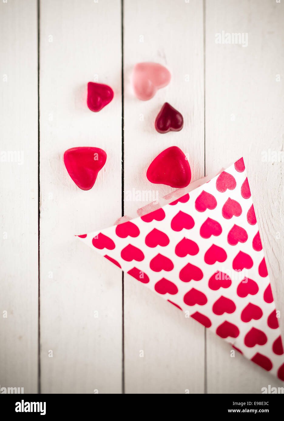 Vista dall'alto di un cono di caramella decorata con cuori rosa fuoriuscita a forma di cuore ad caramelle gommose oltre un legno bianco bordo tabella Foto Stock