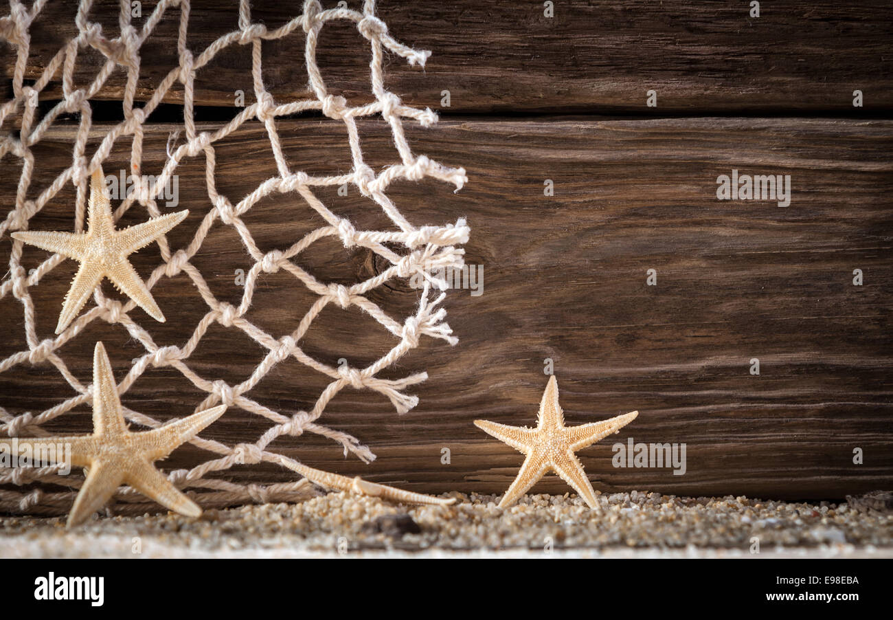 Sfondo nautico con stelle marine e a losanga rete da pesca su assi di legno con un distintivo woodgrain pattern su fresco di sabbia sulla spiaggia con copyspace Foto Stock