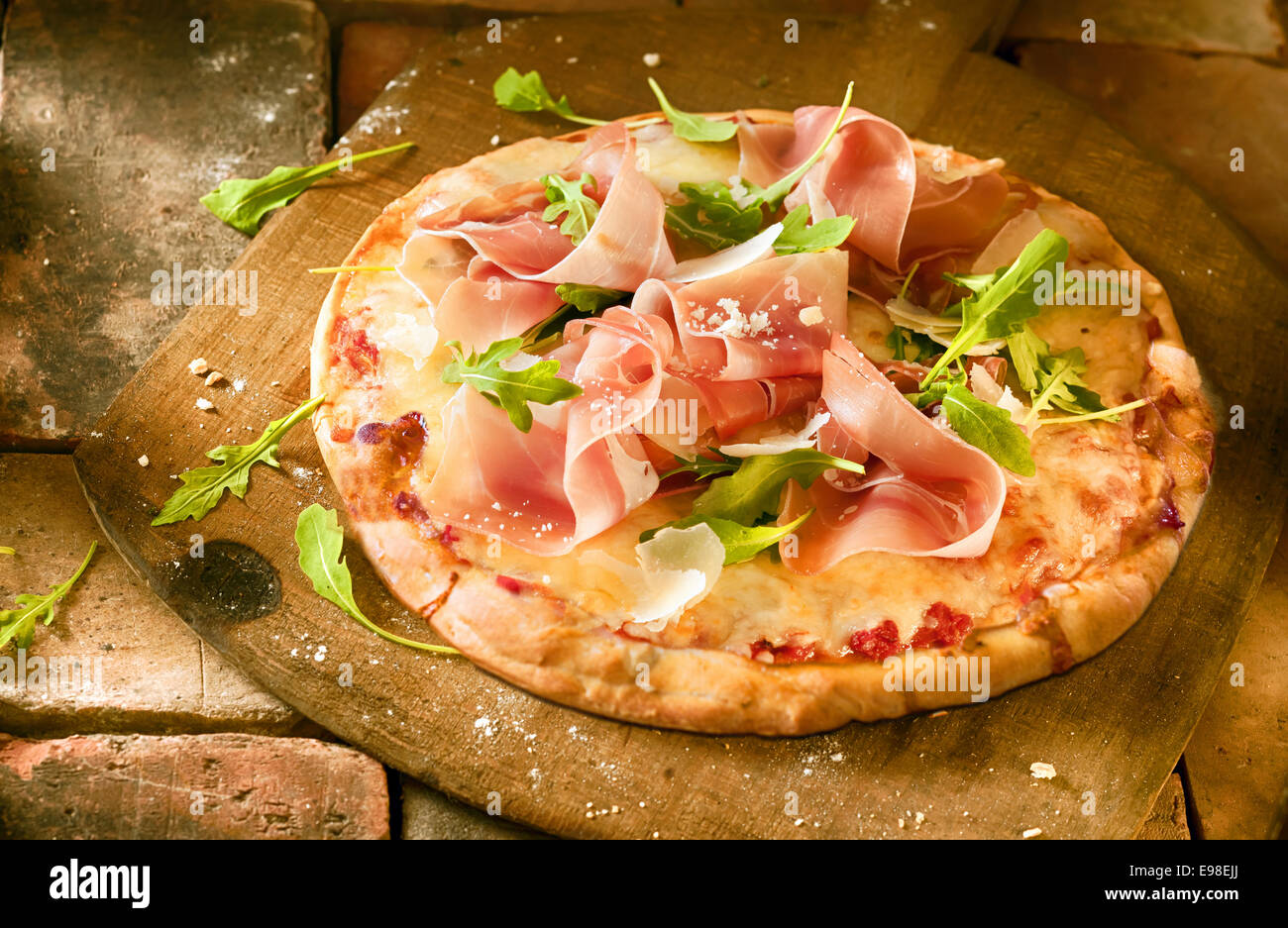 Preparazione di un prosciutto e rucola pizza con fette sottili fette di prosciutto e fresche foglie di rucola disposti su un formaggio e pomodoro base su una paletta di legno ina pizzeria Foto Stock