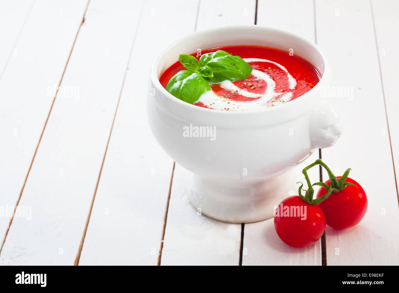 Ciotola di rosso deliziosa minestra di pomodoro e panna guarnito con basilico e cosparsi di pepe e dipinto di bianco per le schede con copyspace Foto Stock